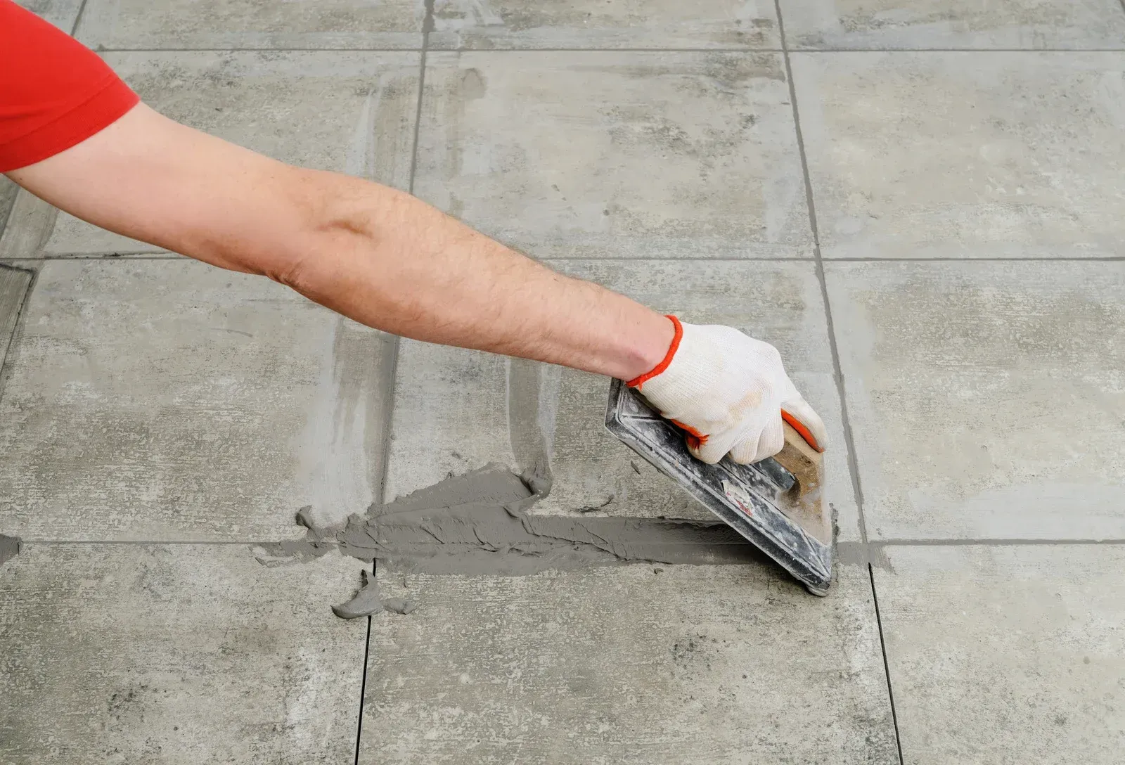 A person is spreading cement on a tiled floor with a trowel.