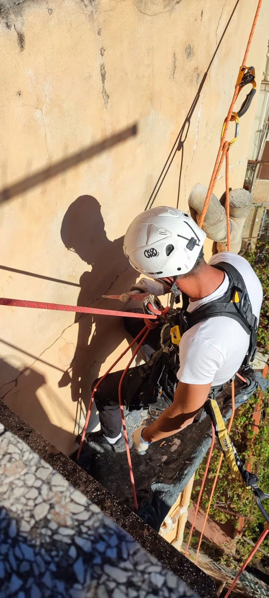 Persona che si cala in corda doppia da un edificio. Indossa un casco bianco e un'imbracatura di sicurezza. Sono visibili corde e carrucole.