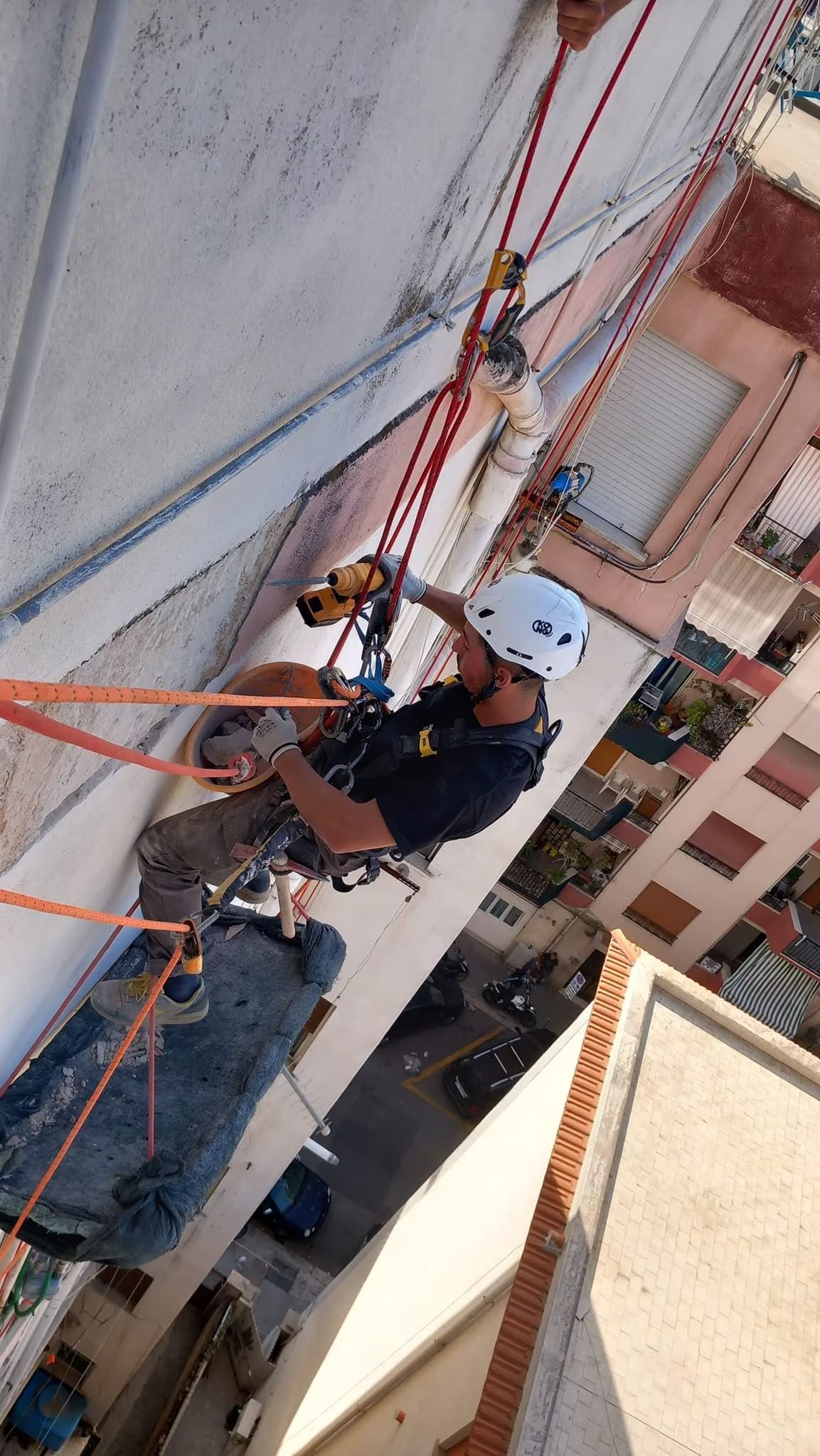 Tecnico di accesso su fune al lavoro sulla facciata di un edificio; indossa un casco e si cala su funi.