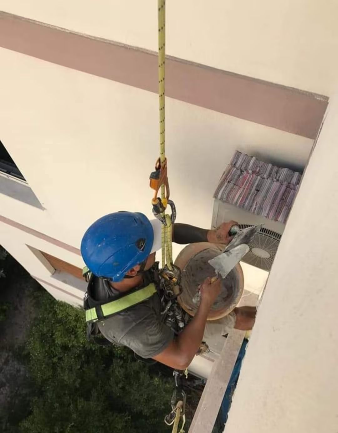 Un operaio edile si cala in corda doppia da un edificio, utilizzando degli attrezzi per lavorare sulla parte esterna.