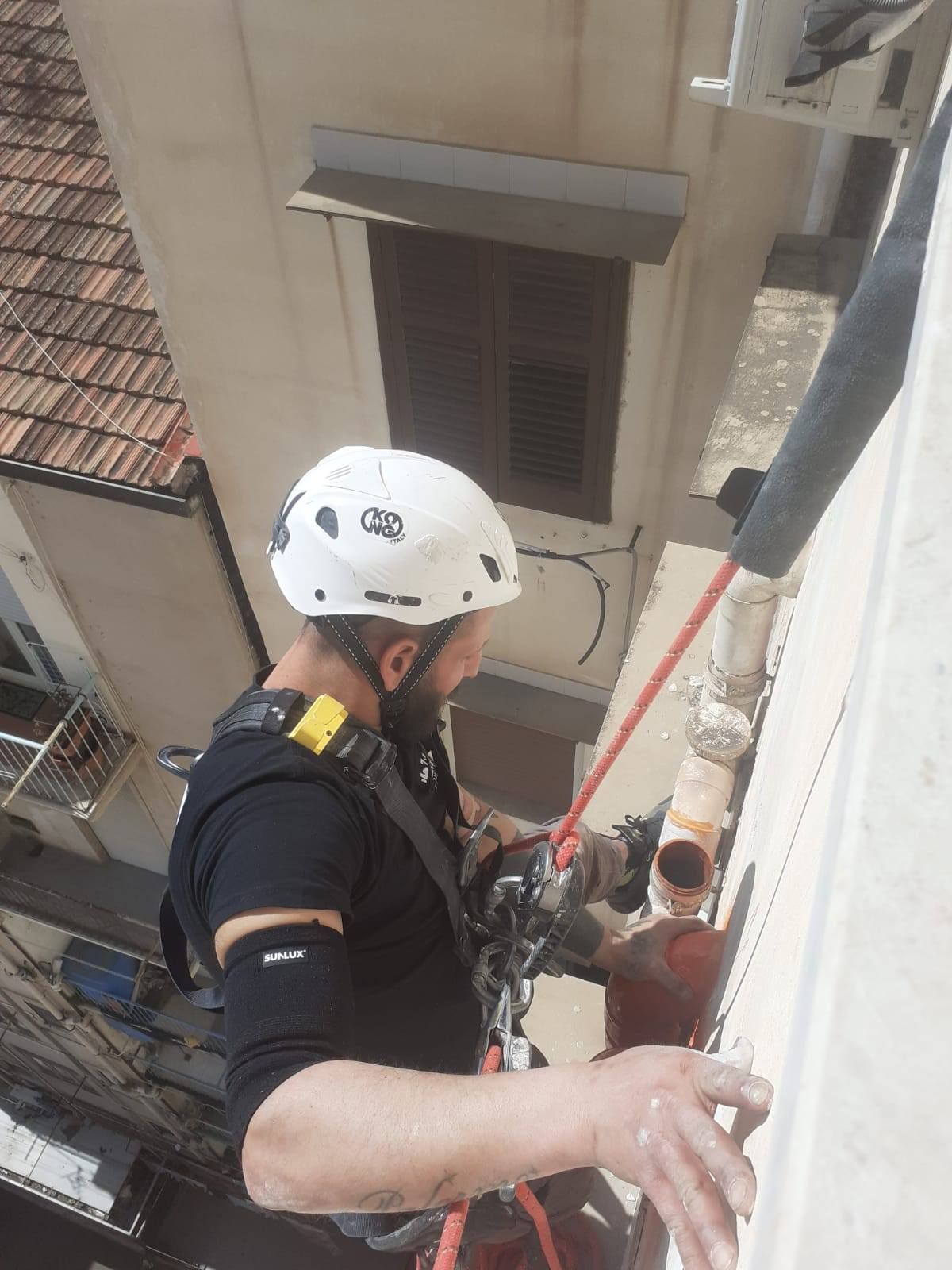 Un uomo con l'attrezzatura di sicurezza si cala in corda doppia lungo il lato di un edificio mentre lavora su un tubo.