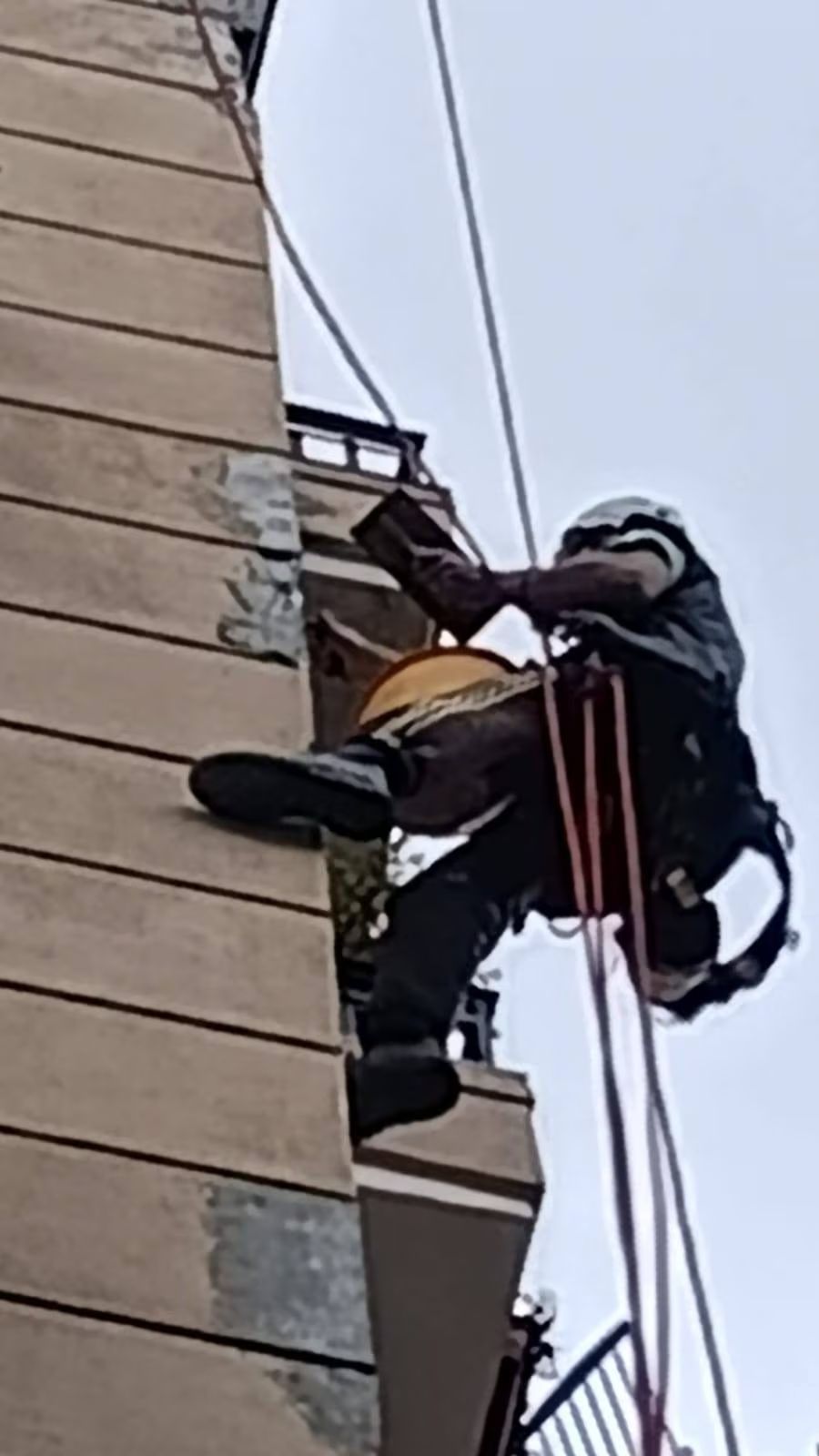 Un uomo imbracato ripara un muro esterno, sospeso tramite delle corde.