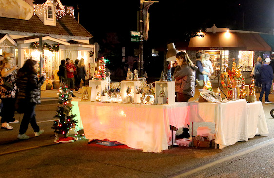 Night street fair with vendor table displaying crafts. People browse. Christmas decorations.