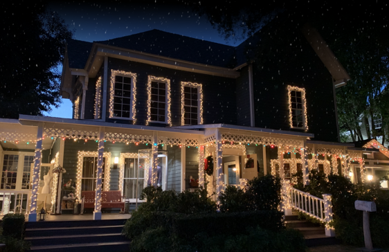 A two-story house at night, decorated with Christmas lights, with falling snow.