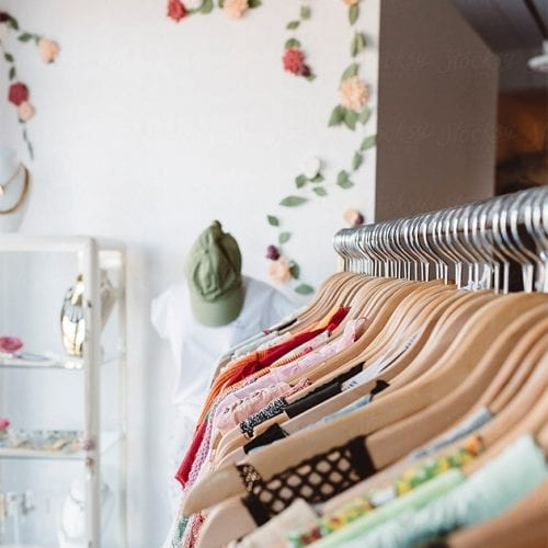 Clothing rack with various brightly colored tops in a boutique with floral wall decorations.