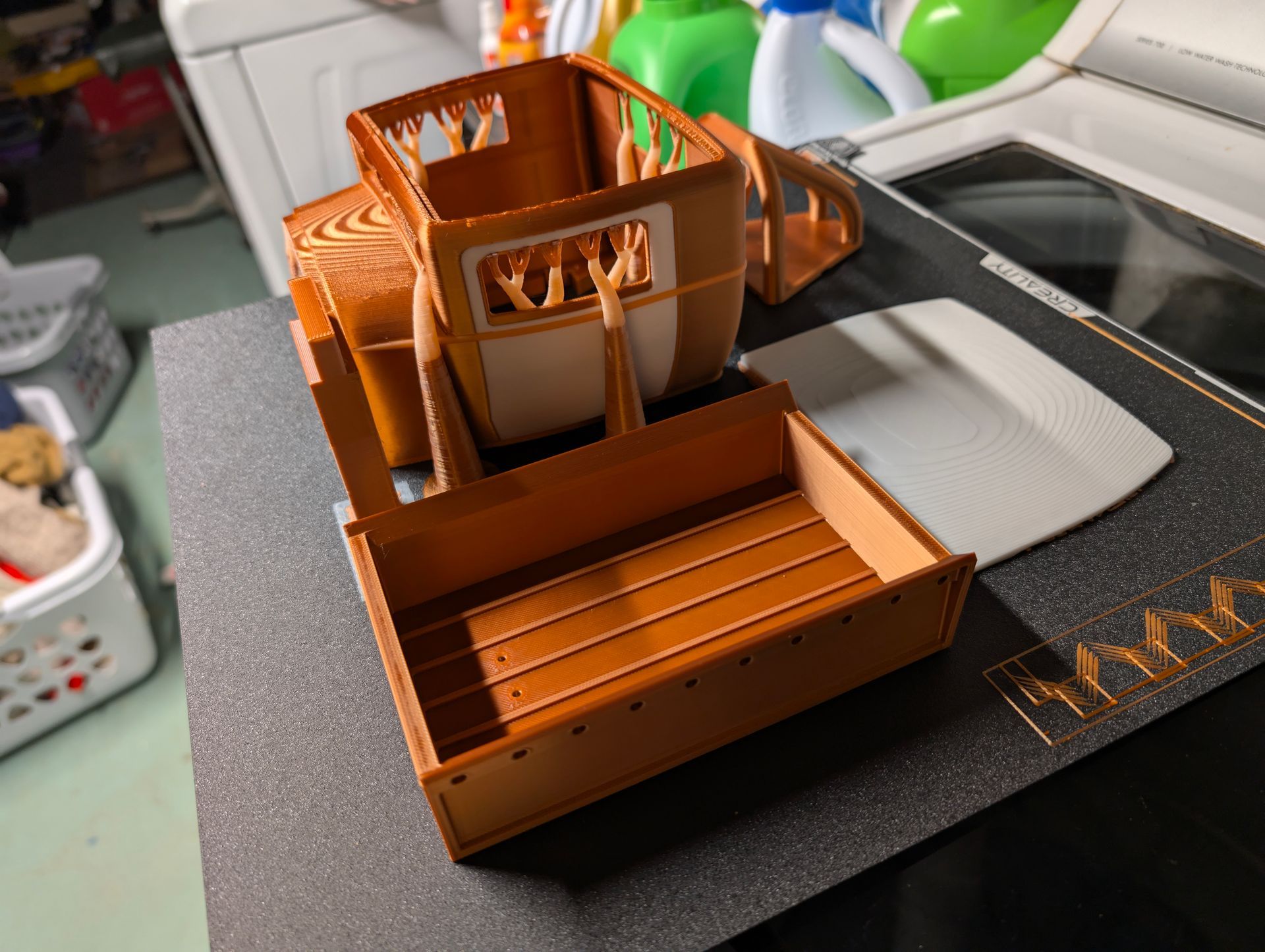 3D-printed model of a brown covered wagon on a dark surface, with white parts and a laundry room background.