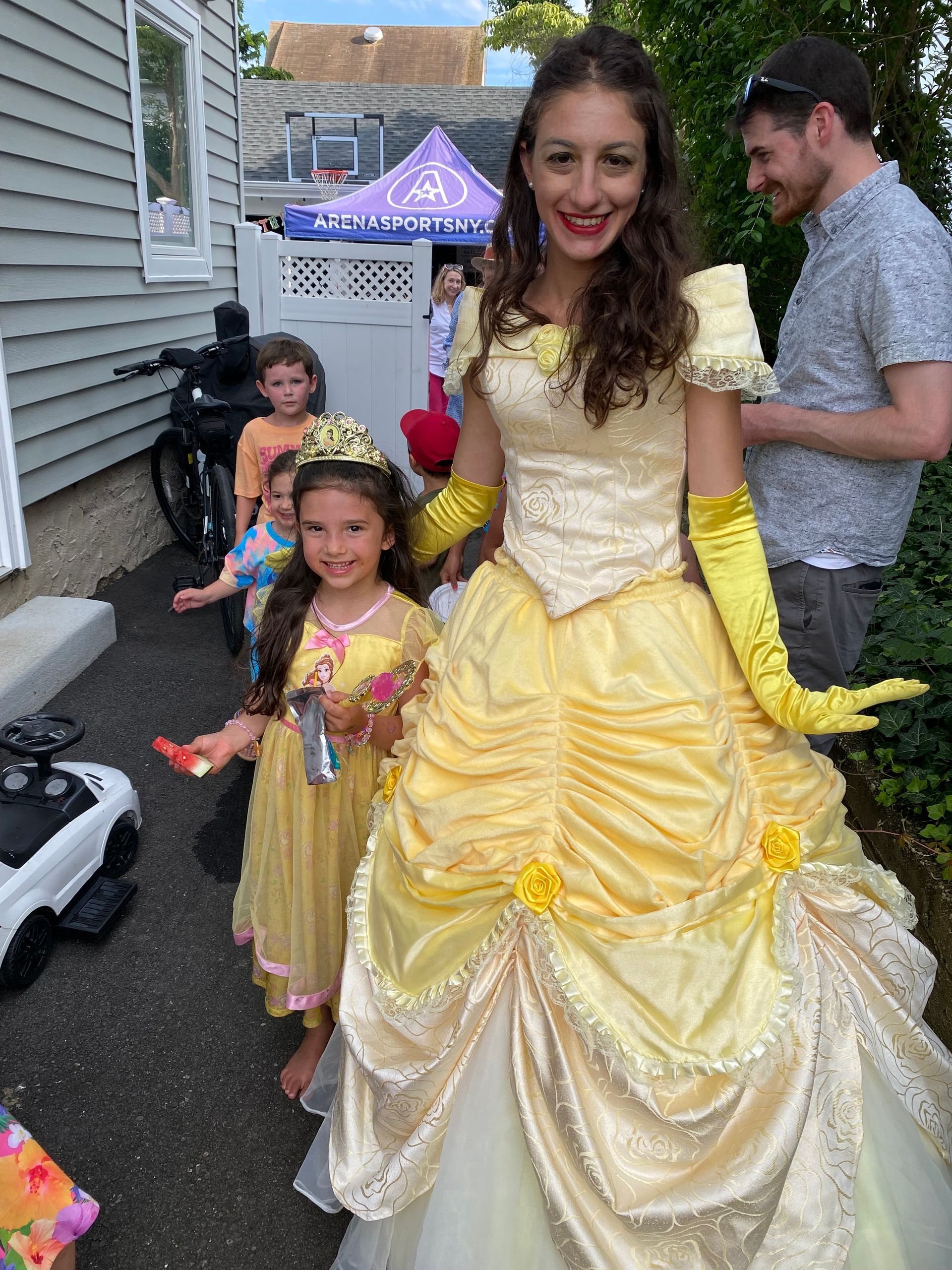 A woman in a yellow dress is standing next to a little girl in a yellow dress.