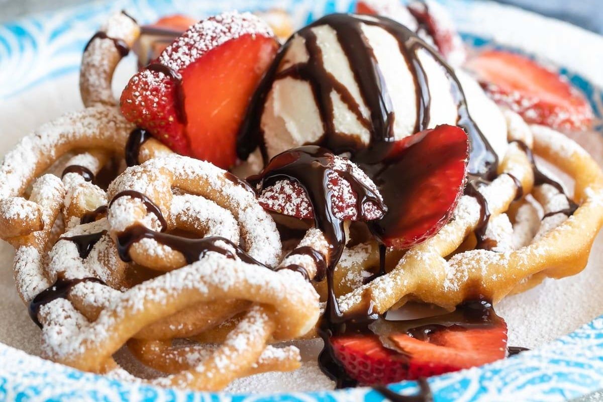 A close up of a plate of funnel cakes with strawberries and ice cream.