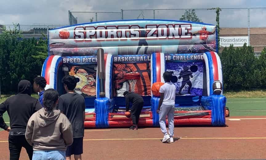 A group of people are standing in front of an inflatable sports zone.