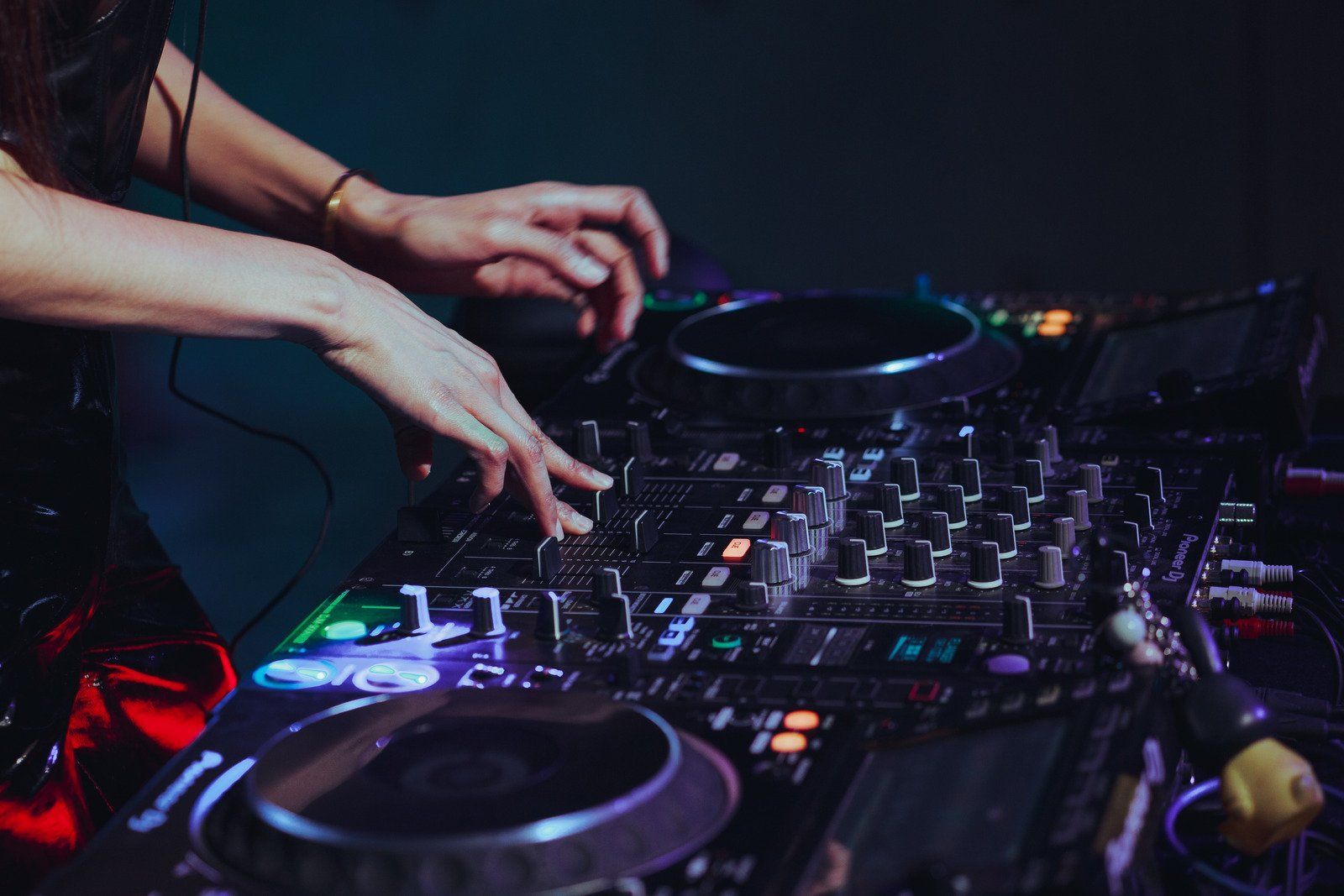 A woman is playing music on a mixer in a dark room.