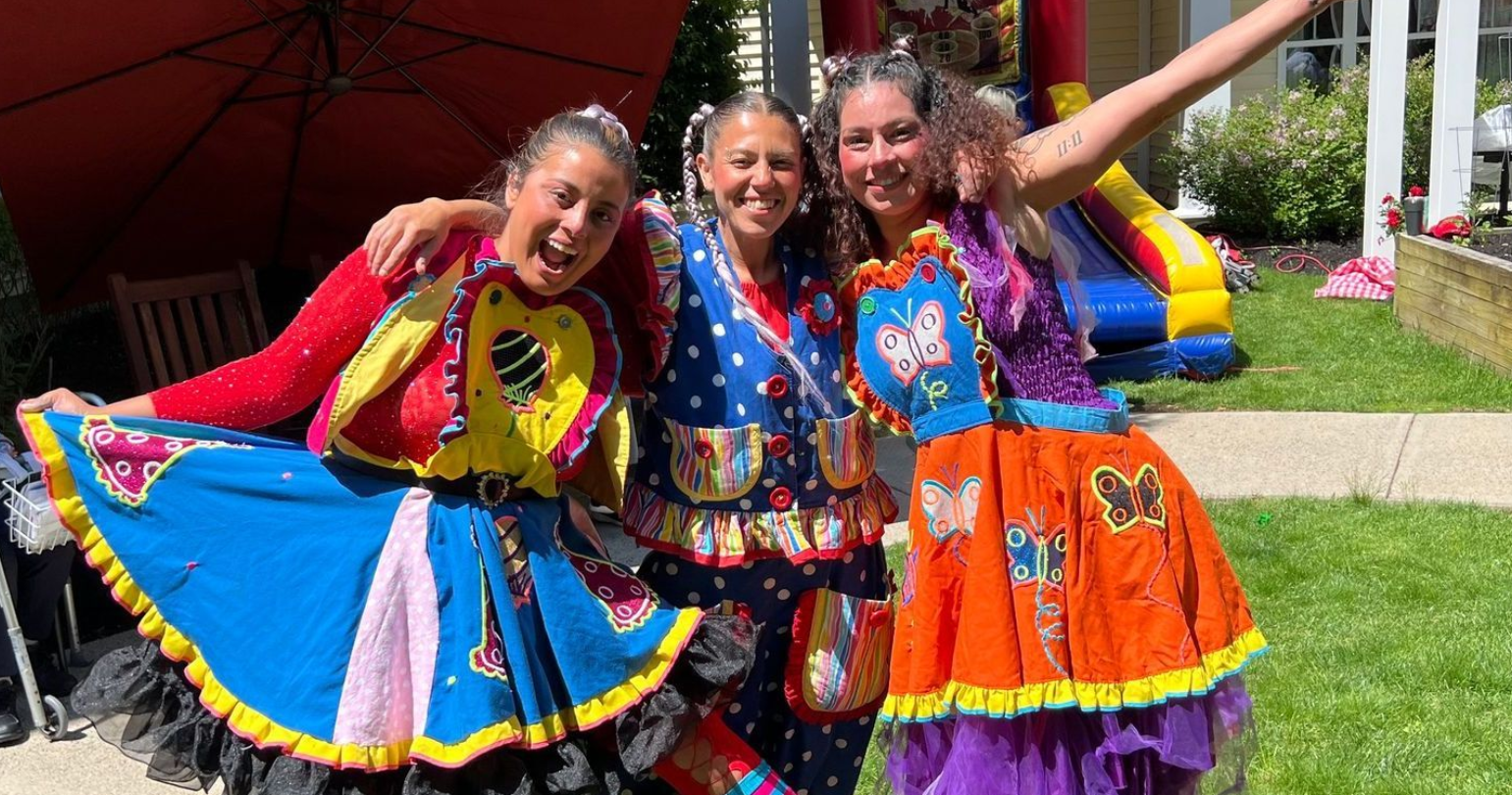 Three women in clown costumes are posing for a picture in front of a house.