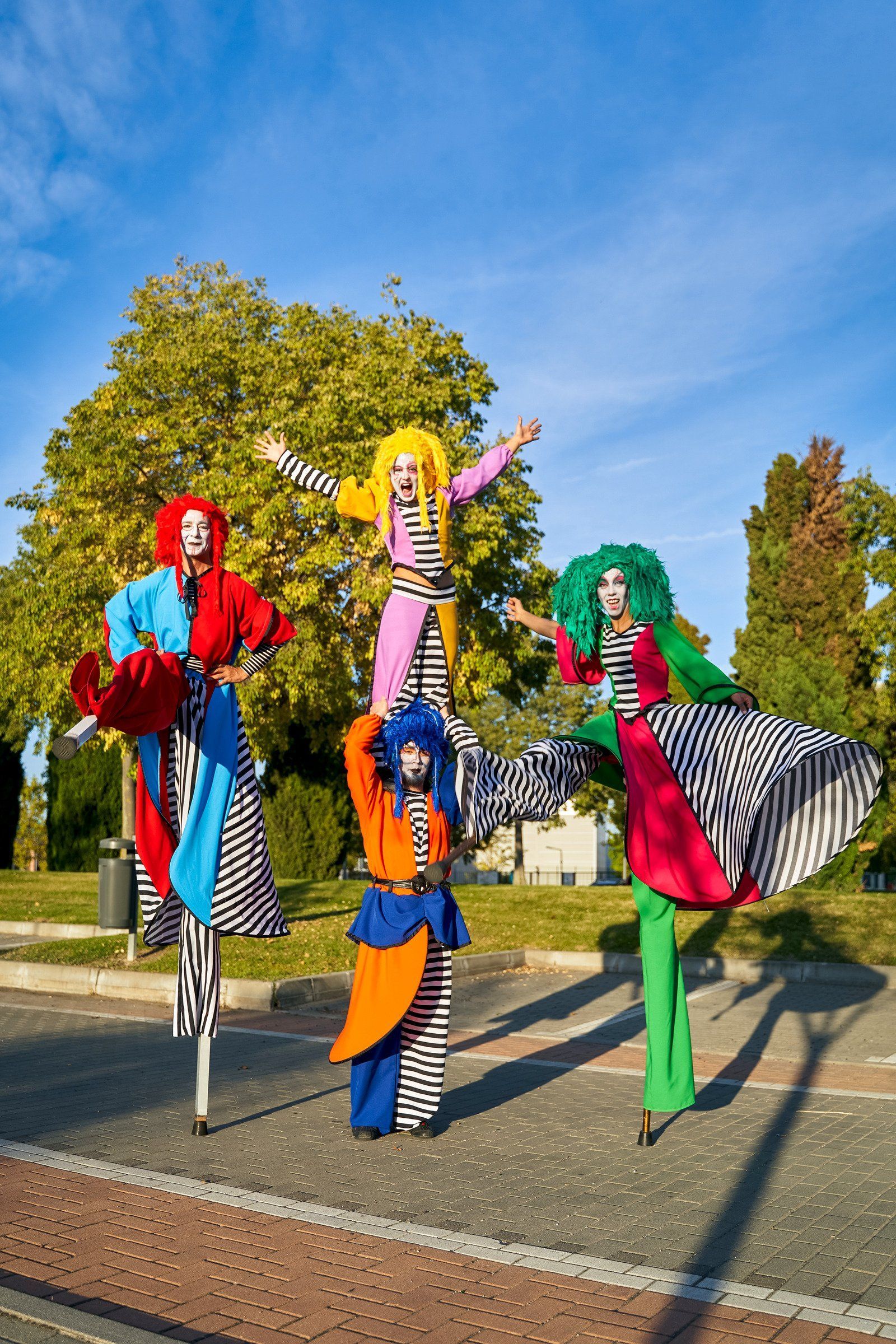 A group of clowns are walking on stilts on a street.