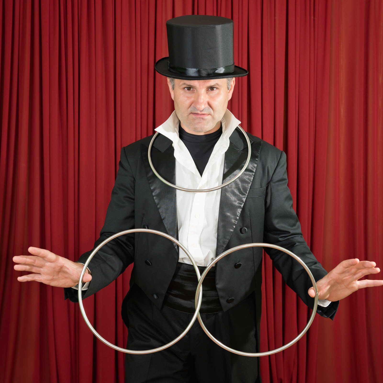 A man in a top hat is holding two rings in his hands
