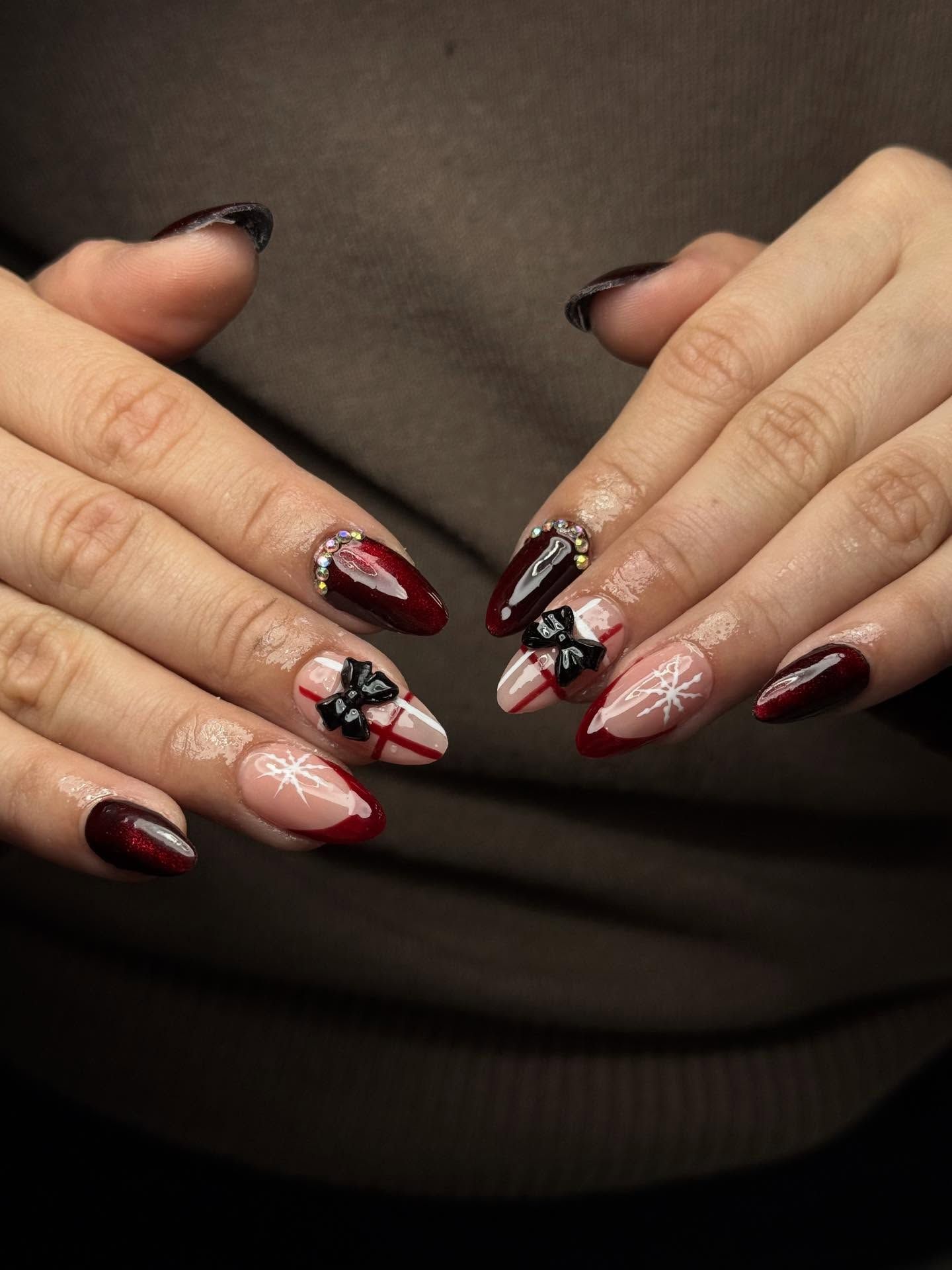 Hands with almond-shaped nails; dark red and neutral base with black bow and snowflake designs.