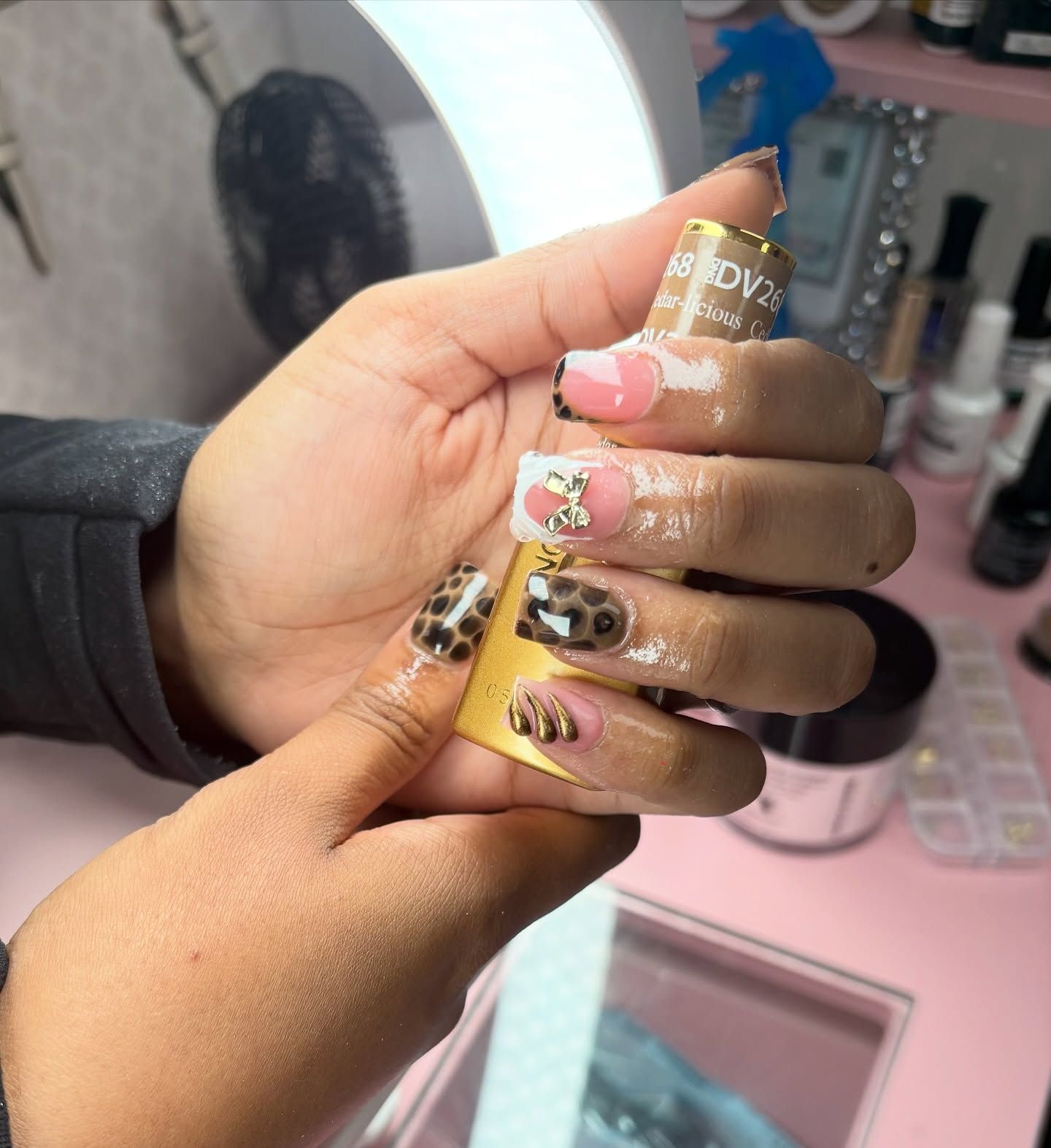 Hand with freshly manicured nails holding nail polish; leopard and French tip designs.