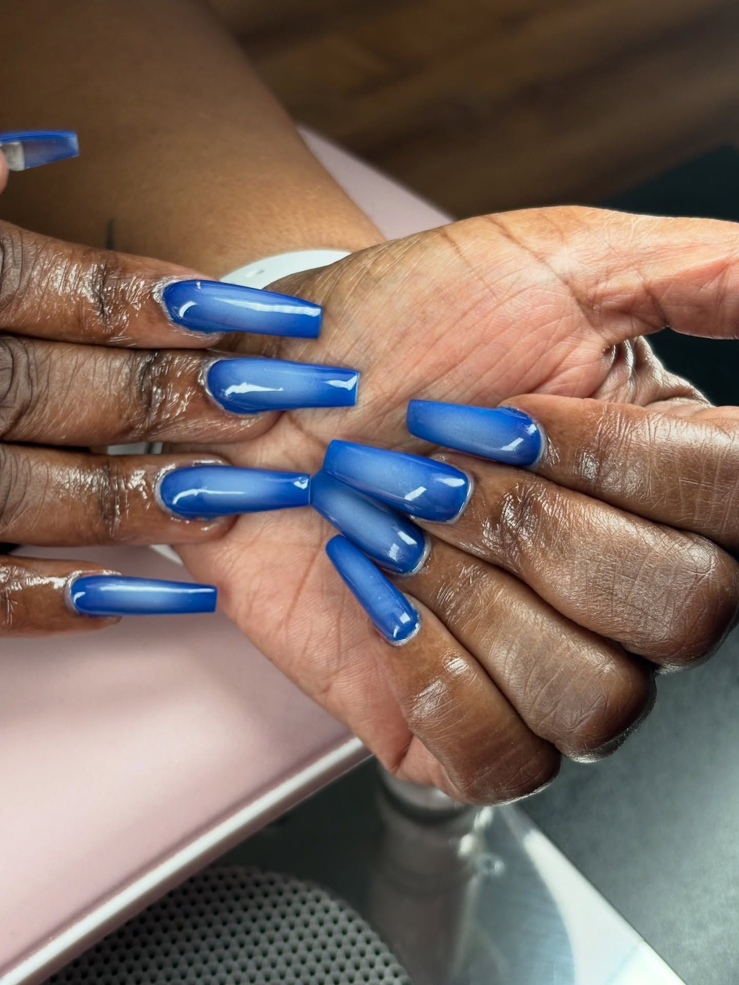 Hands with long, coffin-shaped blue ombre nails. Light catches the shiny surfaces.