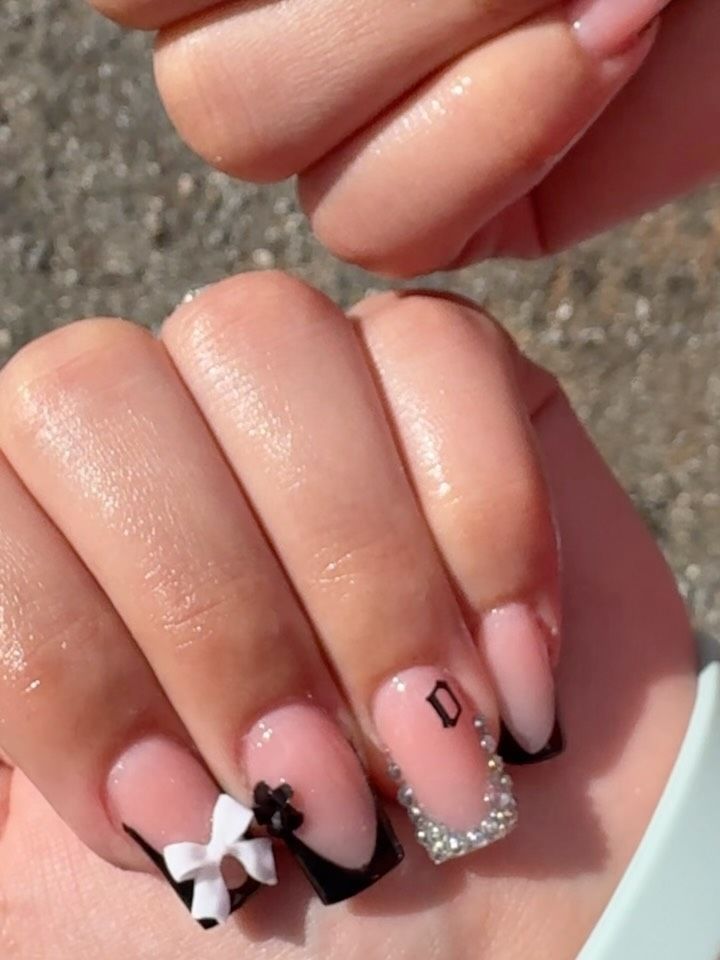 Hand with acrylic nails, black and white tips, bow and jewel details,