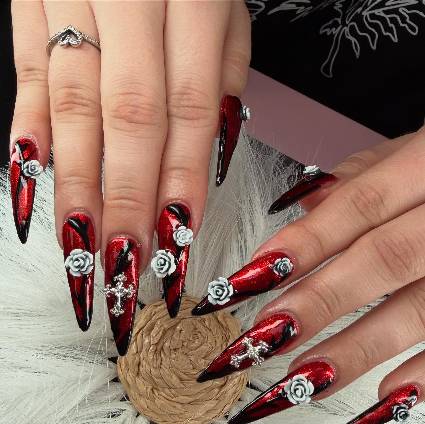 Close-up of hands with long, red and black stiletto nails, silver crosses and roses.