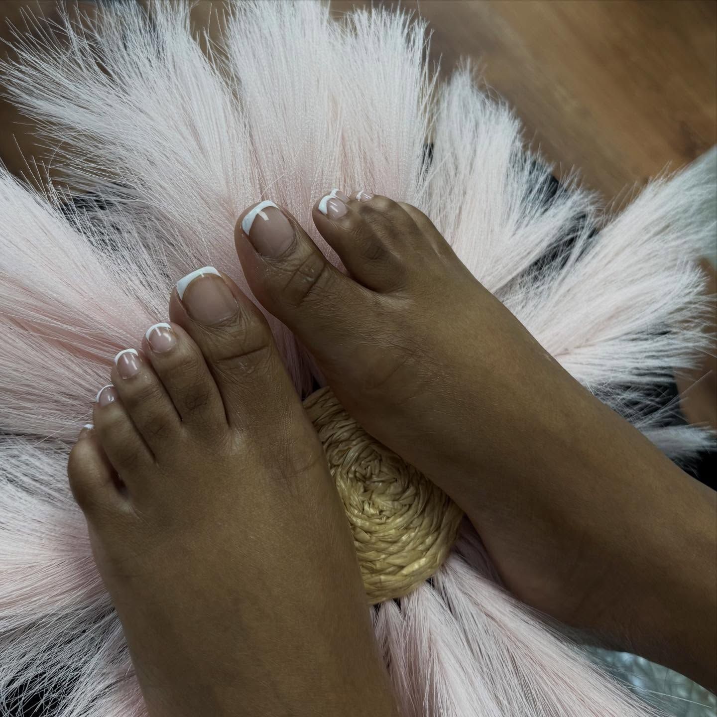 Feet with French-tipped toenails resting on a pink flower-shaped cushion.