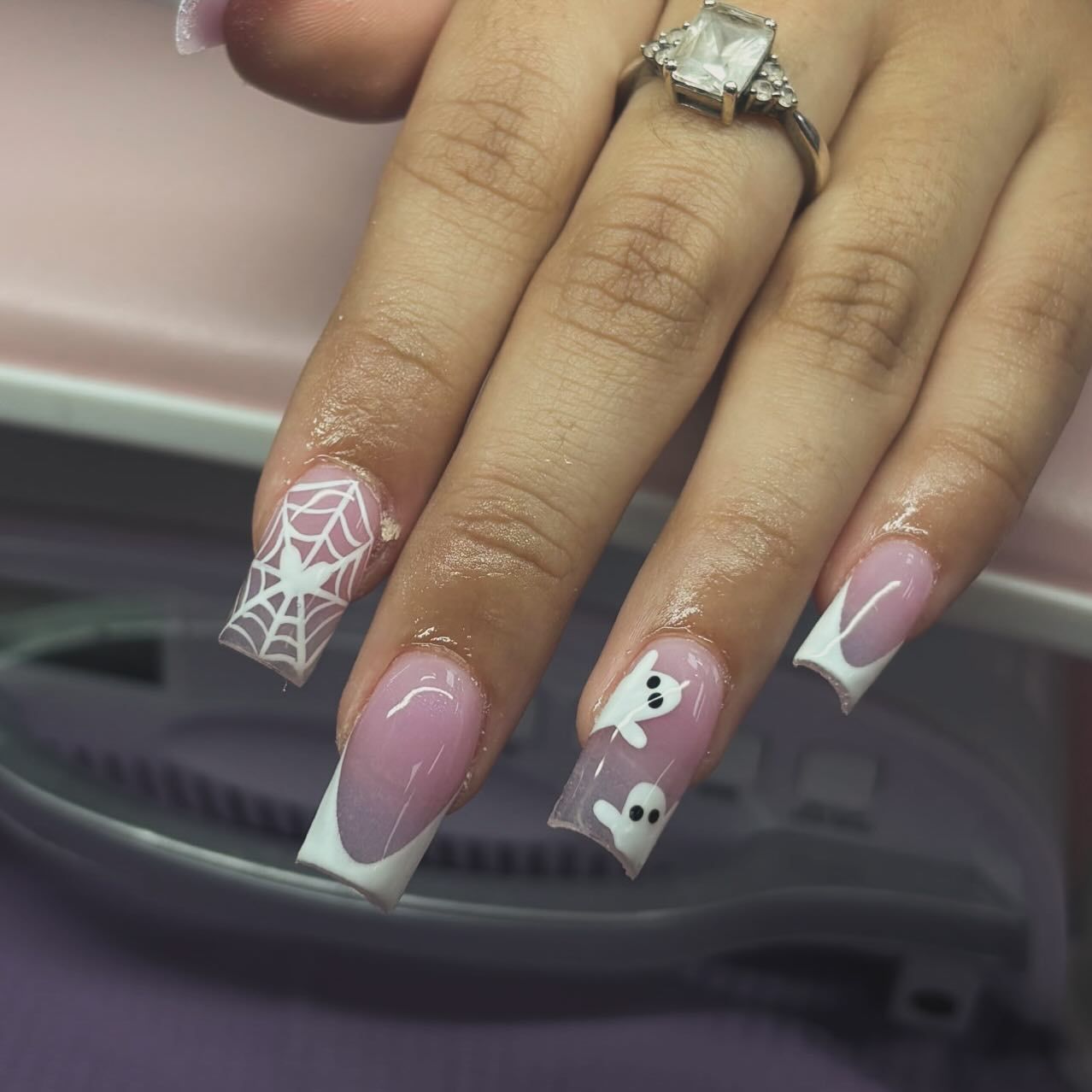 Hand with square-shaped French tip nails, including Halloween designs: spiderweb and ghosts.