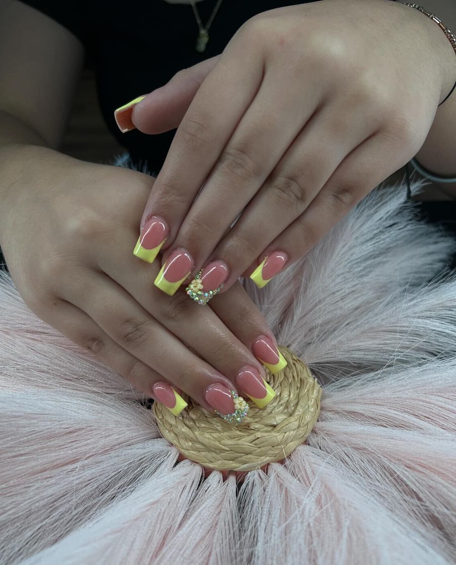 Hands with pink and yellow French tip nails, adorned with a small jeweled accent.