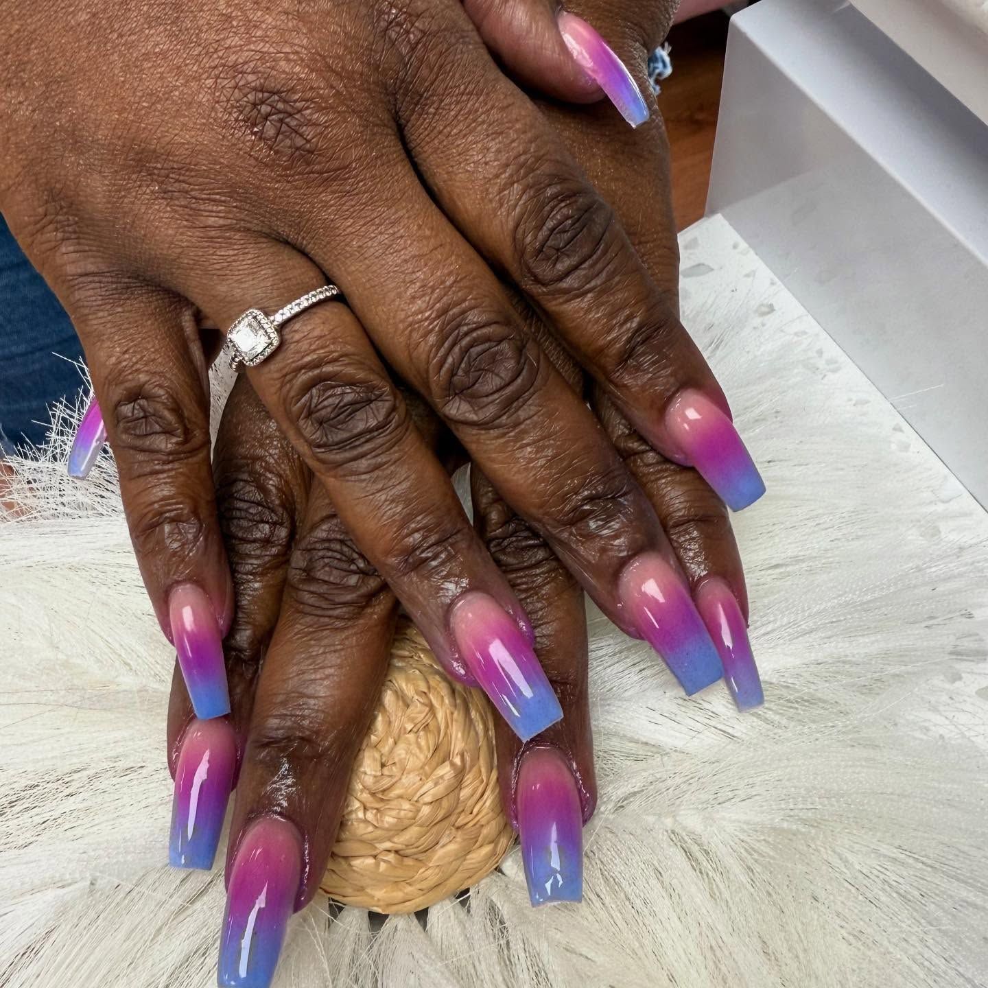 Hands with ombre nail design, transitioning from pink to blue. One hand features a ring.