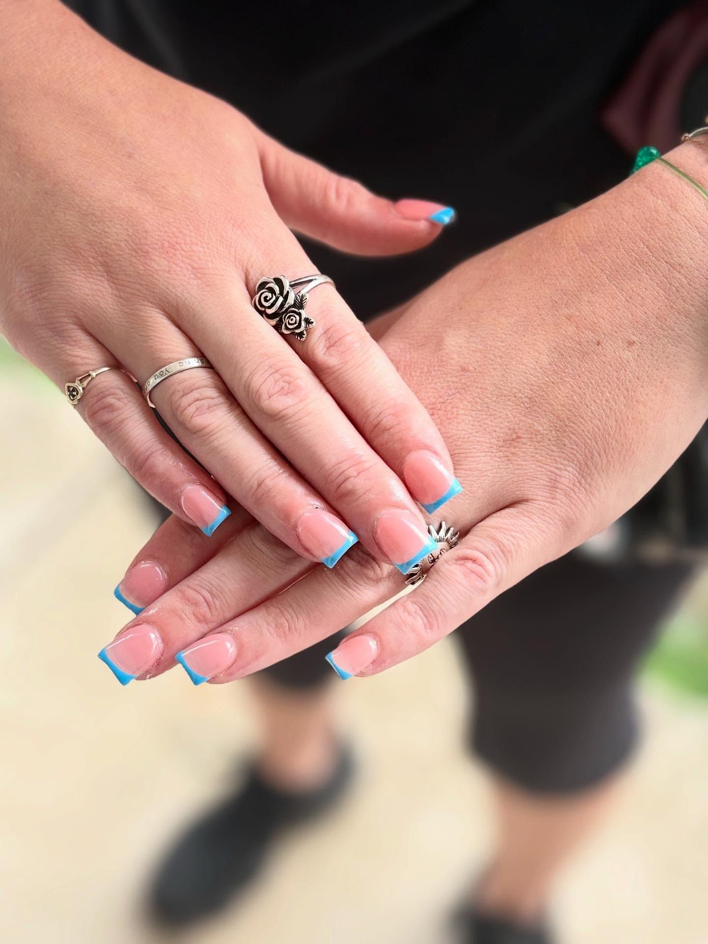 Hands with square-shaped nails painted with a light blue french tip. Silver rings adorn the fingers.