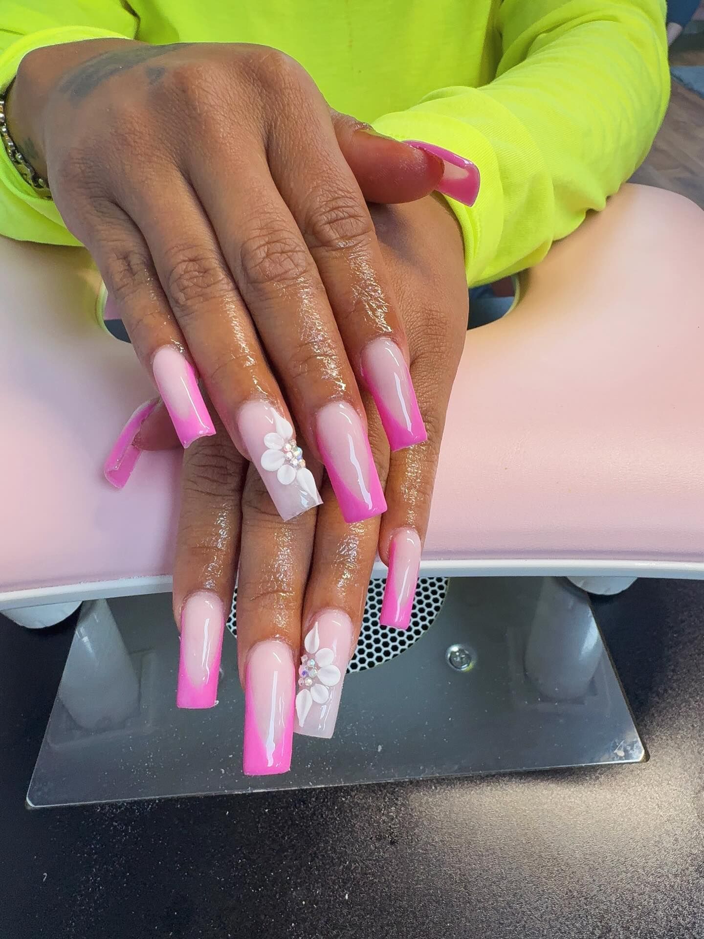 Hands with long, pink and white ombre nails, decorated with white floral accents.