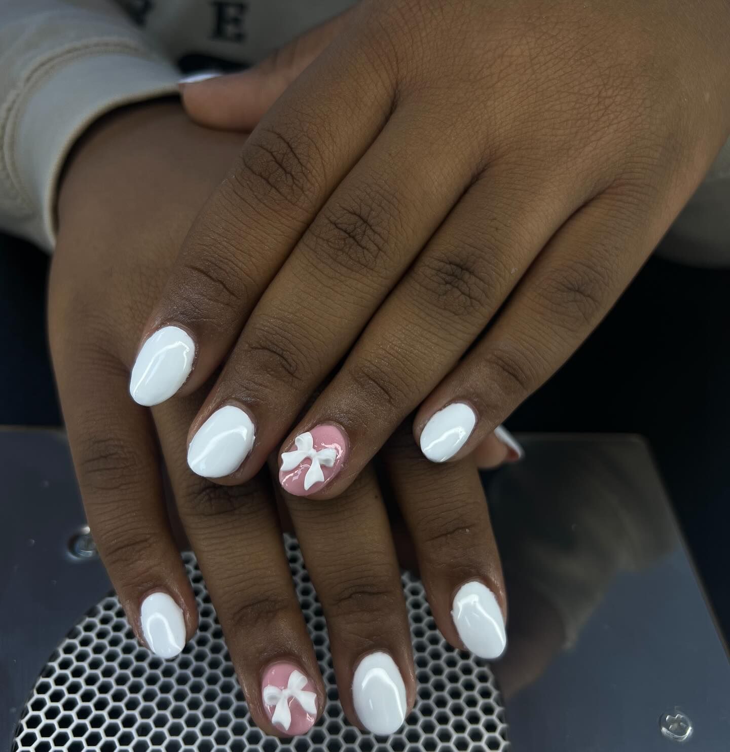 Hands with white oval nails, one with pink bow accent.