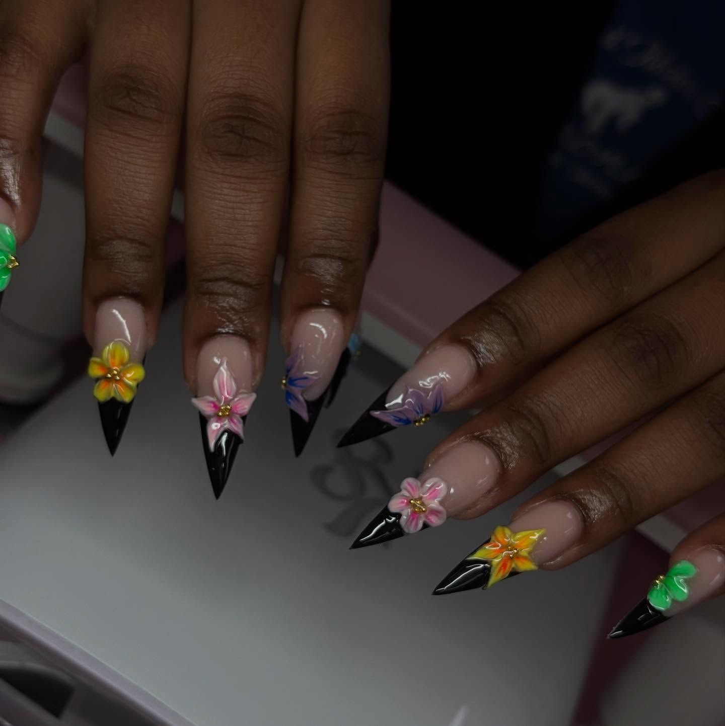 Long black stiletto nails with 3D floral accents and a French tip design.