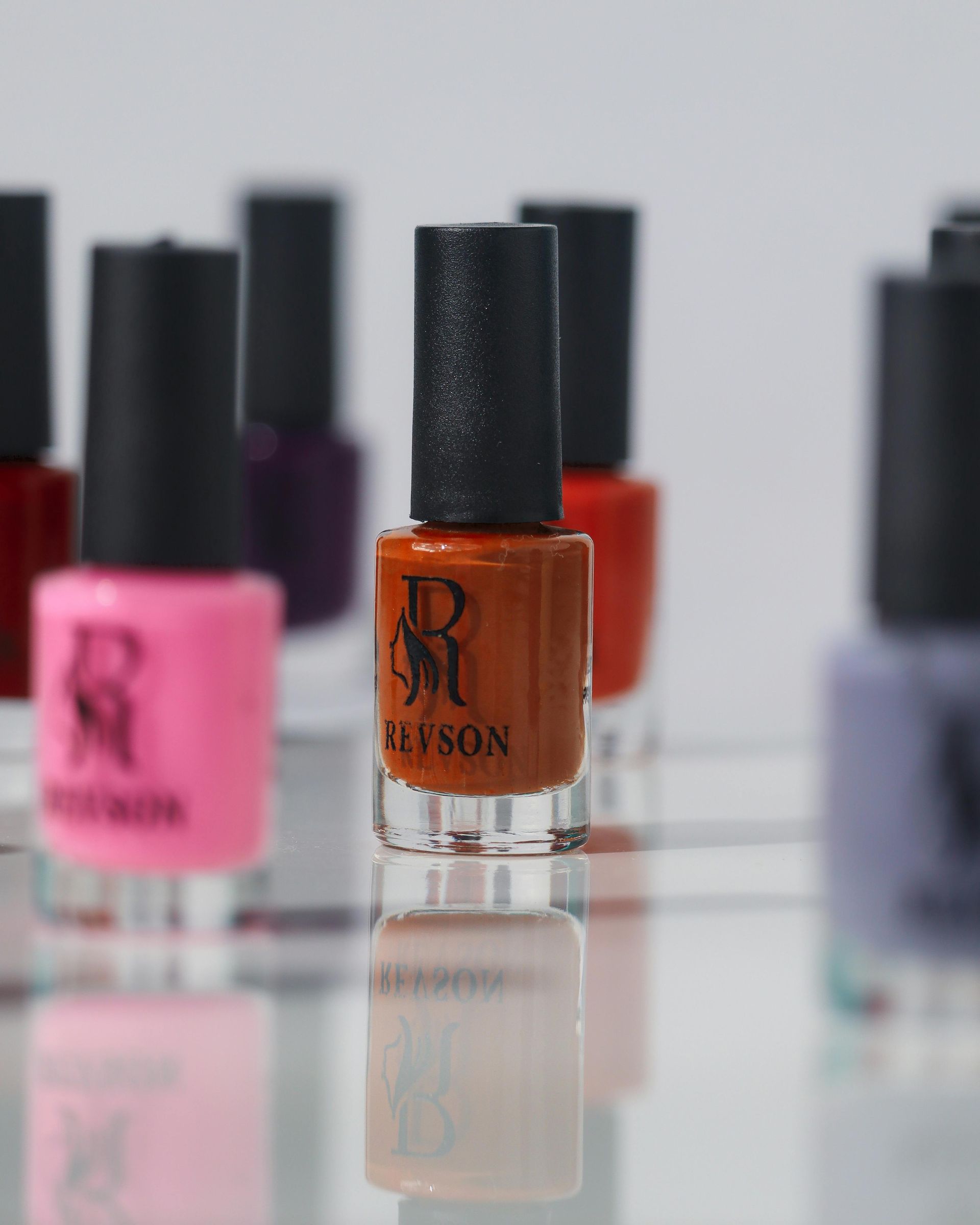 Nail polish bottles in various colors on a clear display, with a focus on an orange bottle.