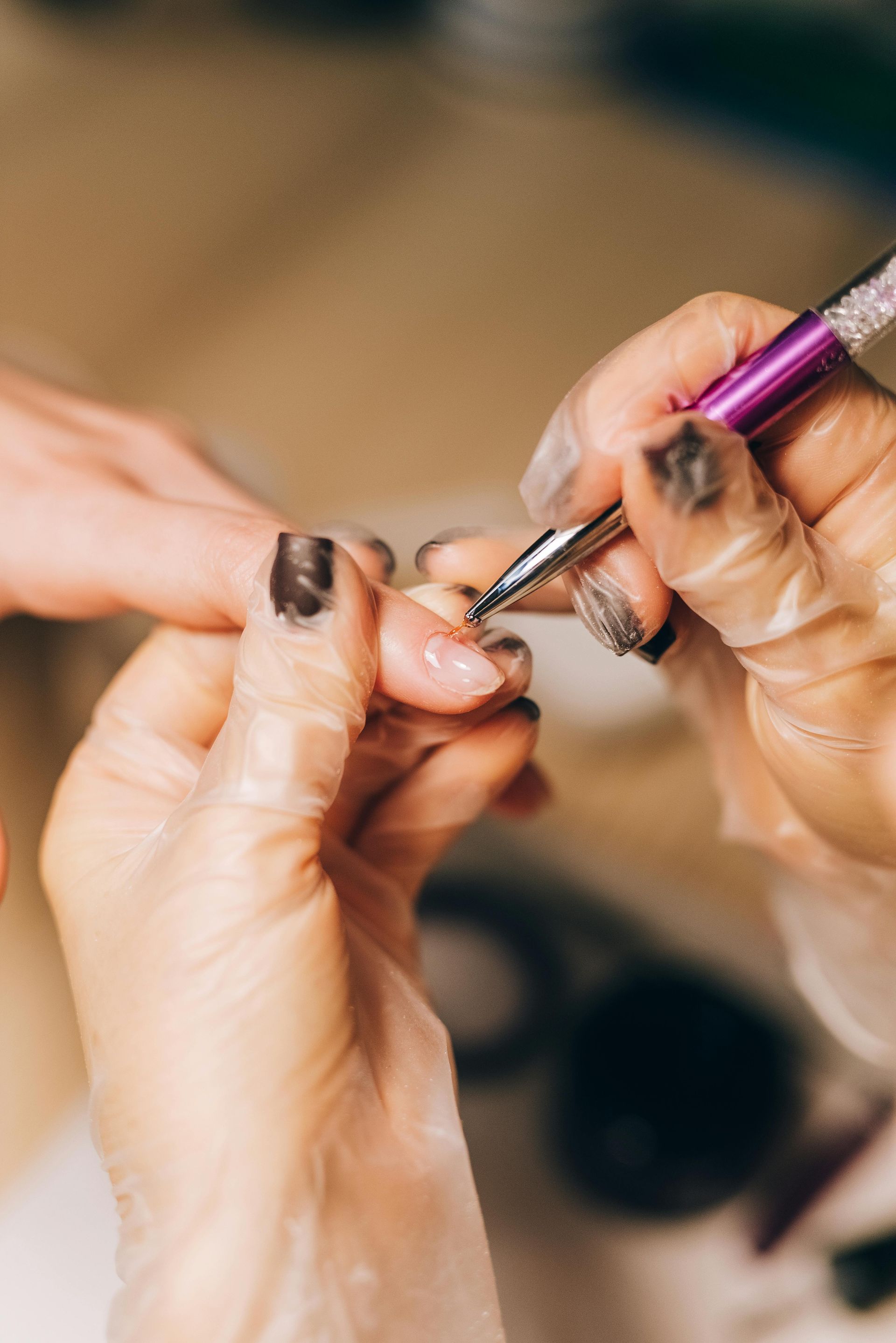 Person's hand getting nail art applied; another gloved hand holds a tool.