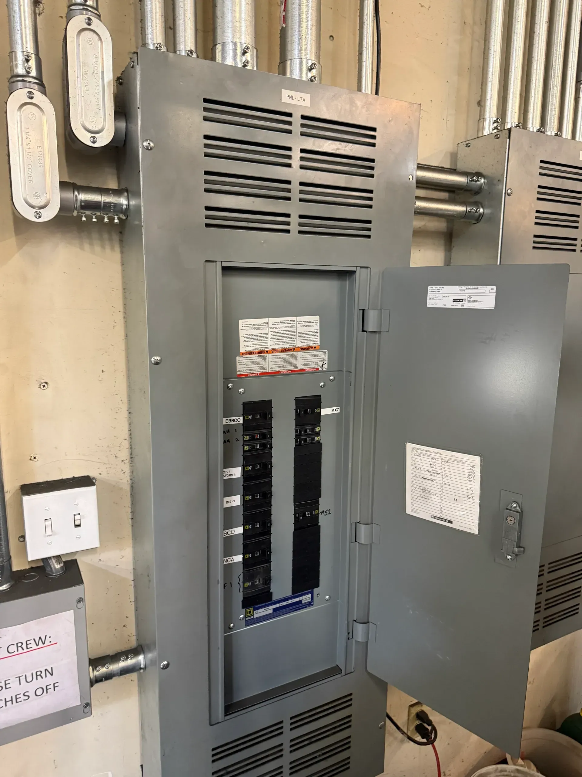 A large electrical box with the door open is sitting on a wall.