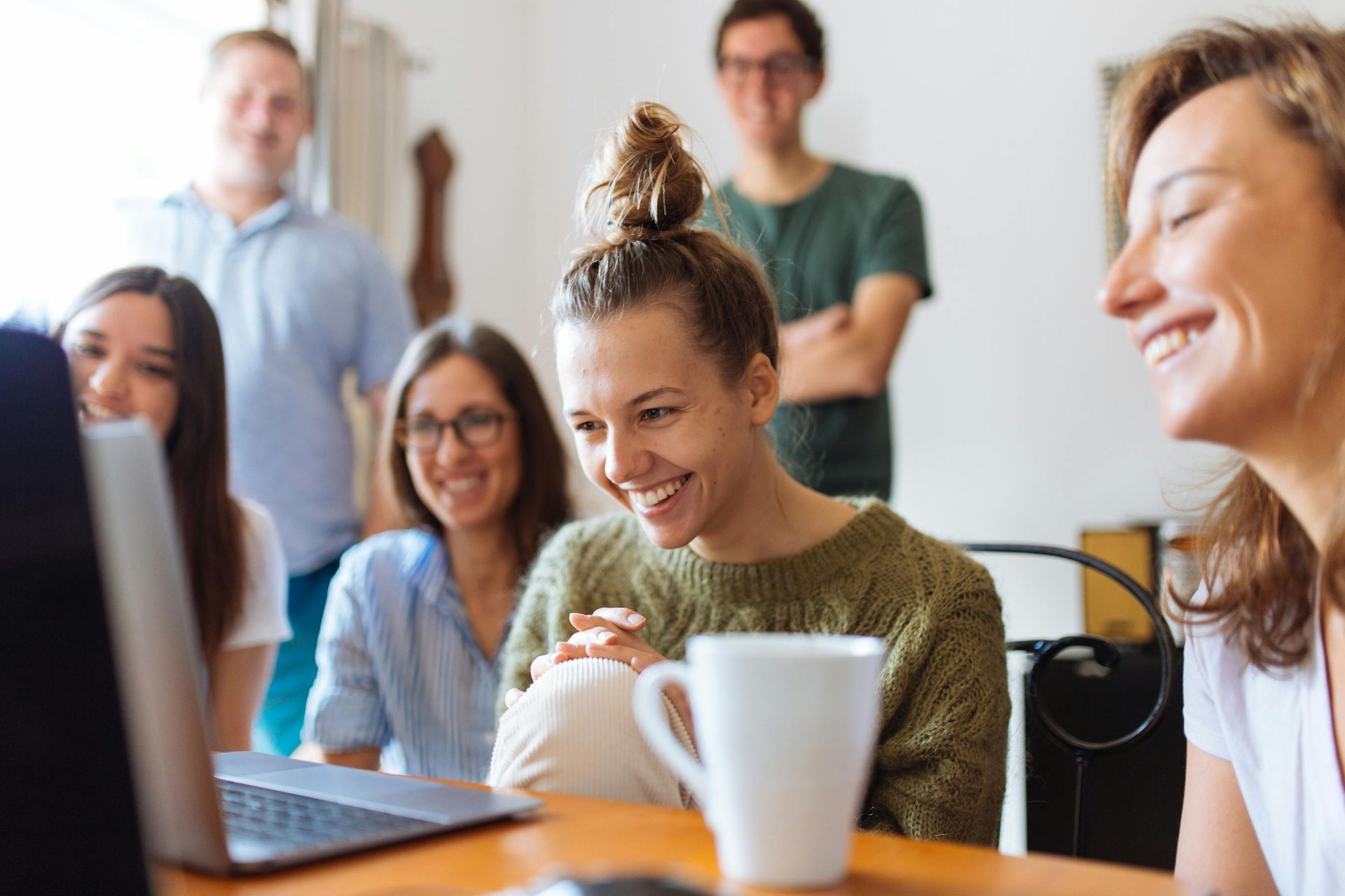 A group of people are sitting around a table looking at a laptop computer.