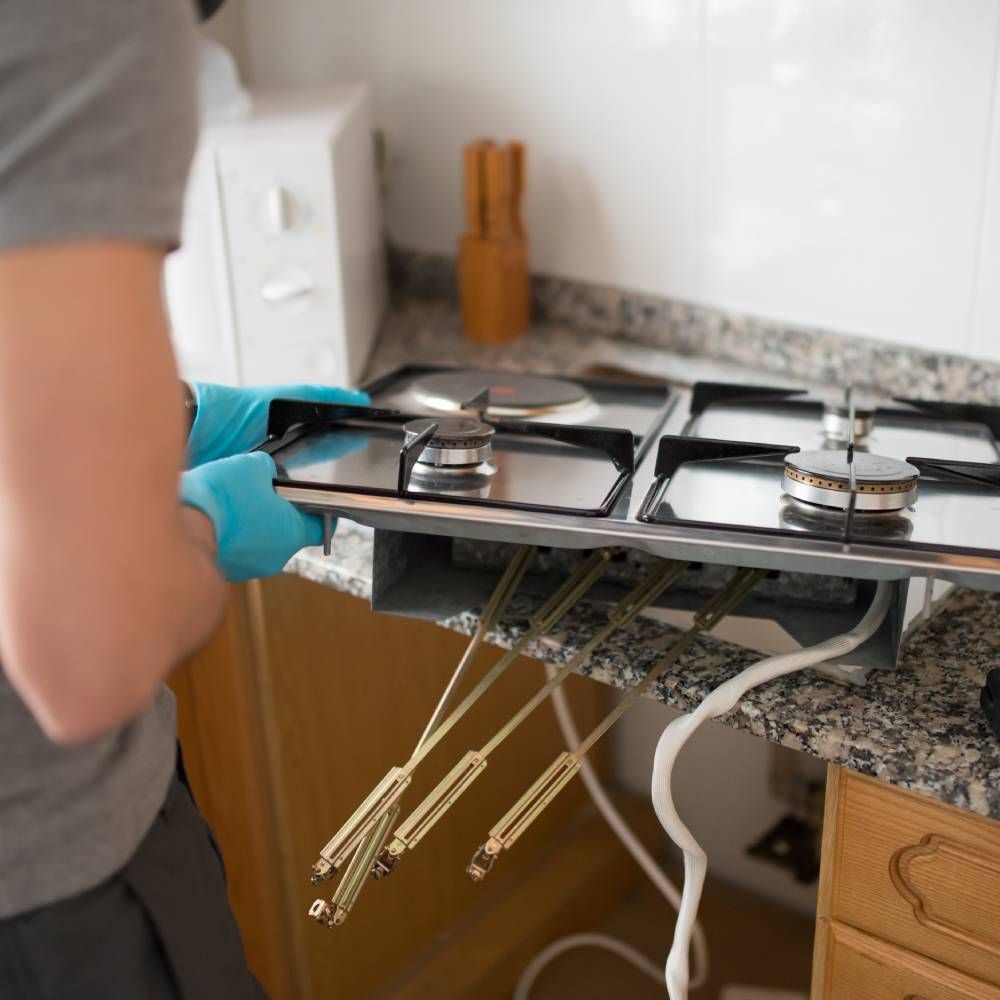 A man is fixing a gas stove in a kitchen.