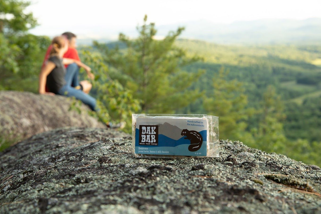 A couple is sitting on top of a rock with a snack bar.