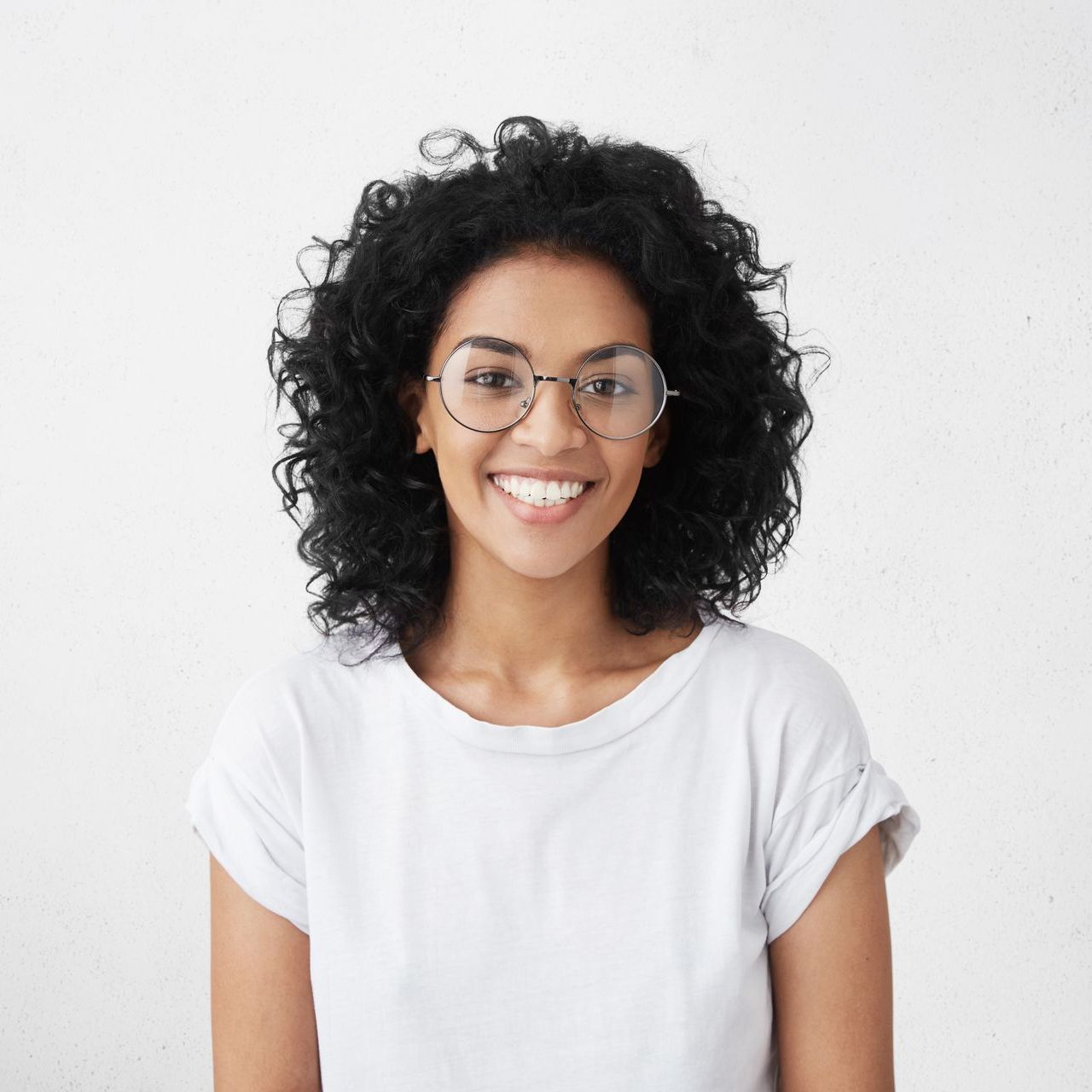 A woman wearing glasses and a white shirt is smiling.