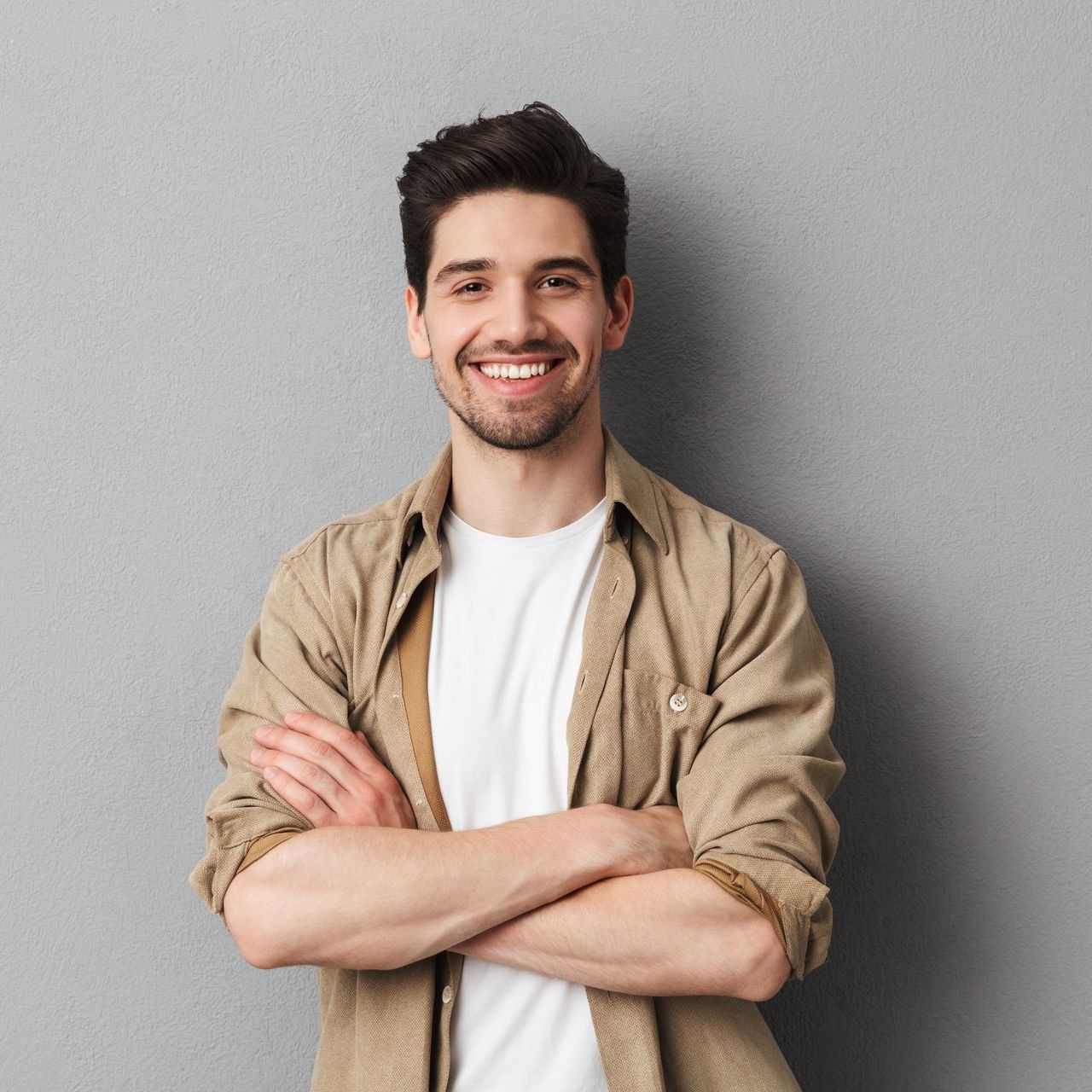 A young man is standing with his arms crossed and smiling.