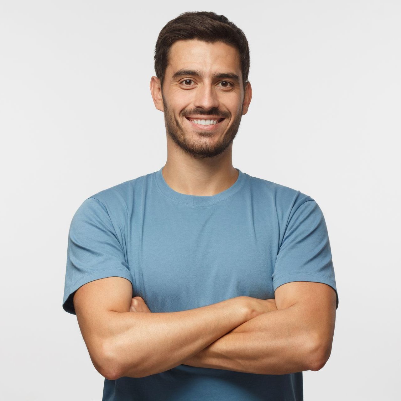 A man in a blue shirt is smiling with his arms crossed