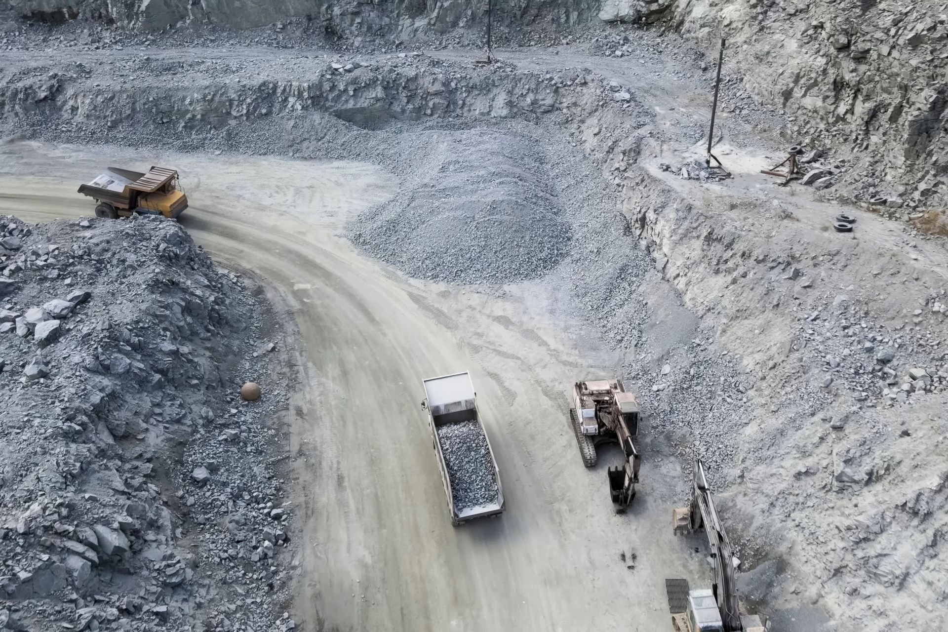 Mining trucks and excavators on a winding dirt road in a gray quarry.