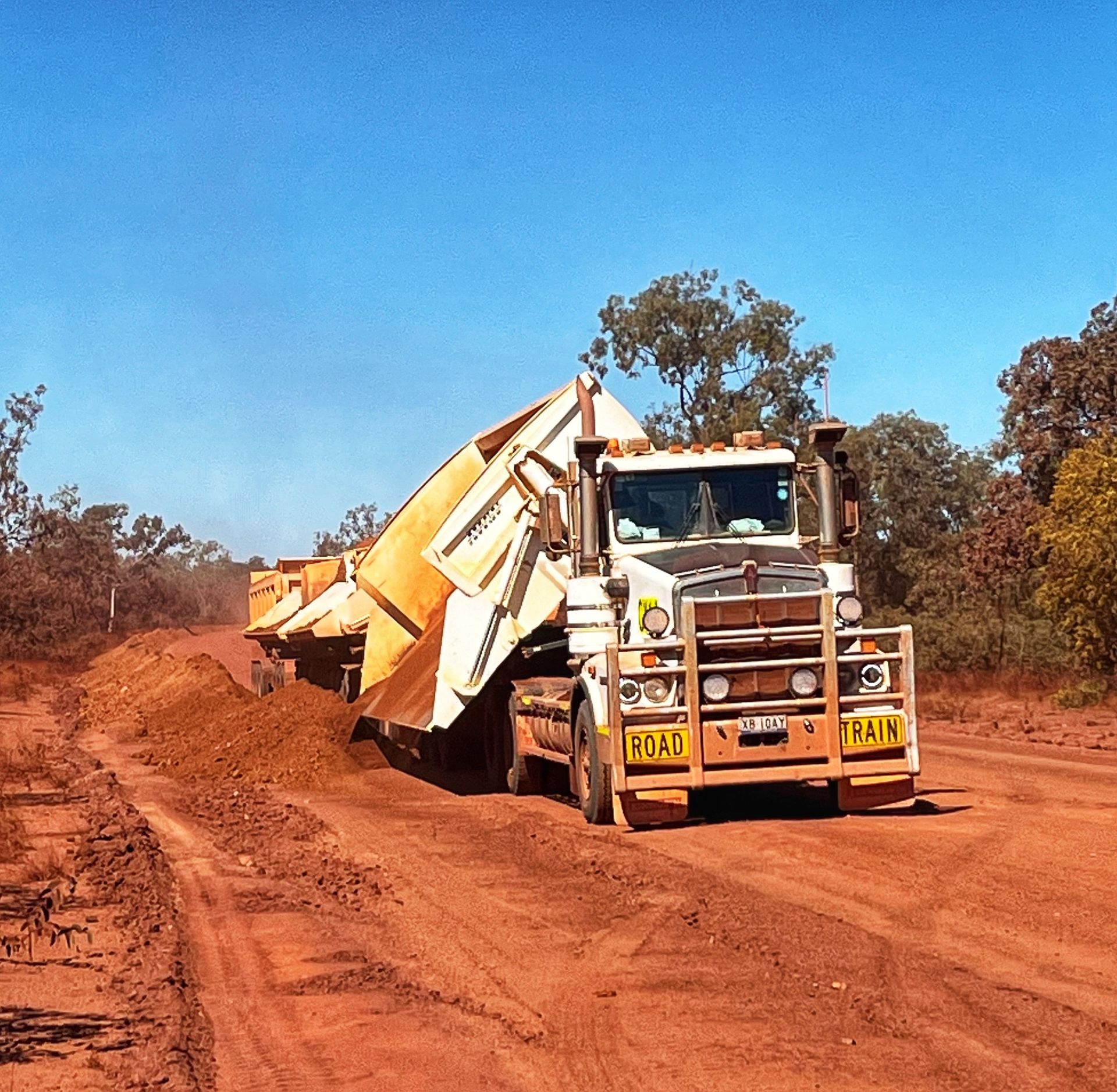 White dump truck hauling dirt on a red dirt road under a clear blue sky