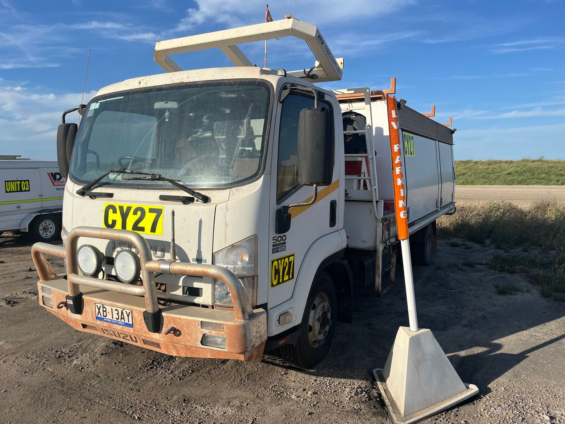 White utility truck with CY27 on the front, parked beside a concrete barrier in a rural roadside area.