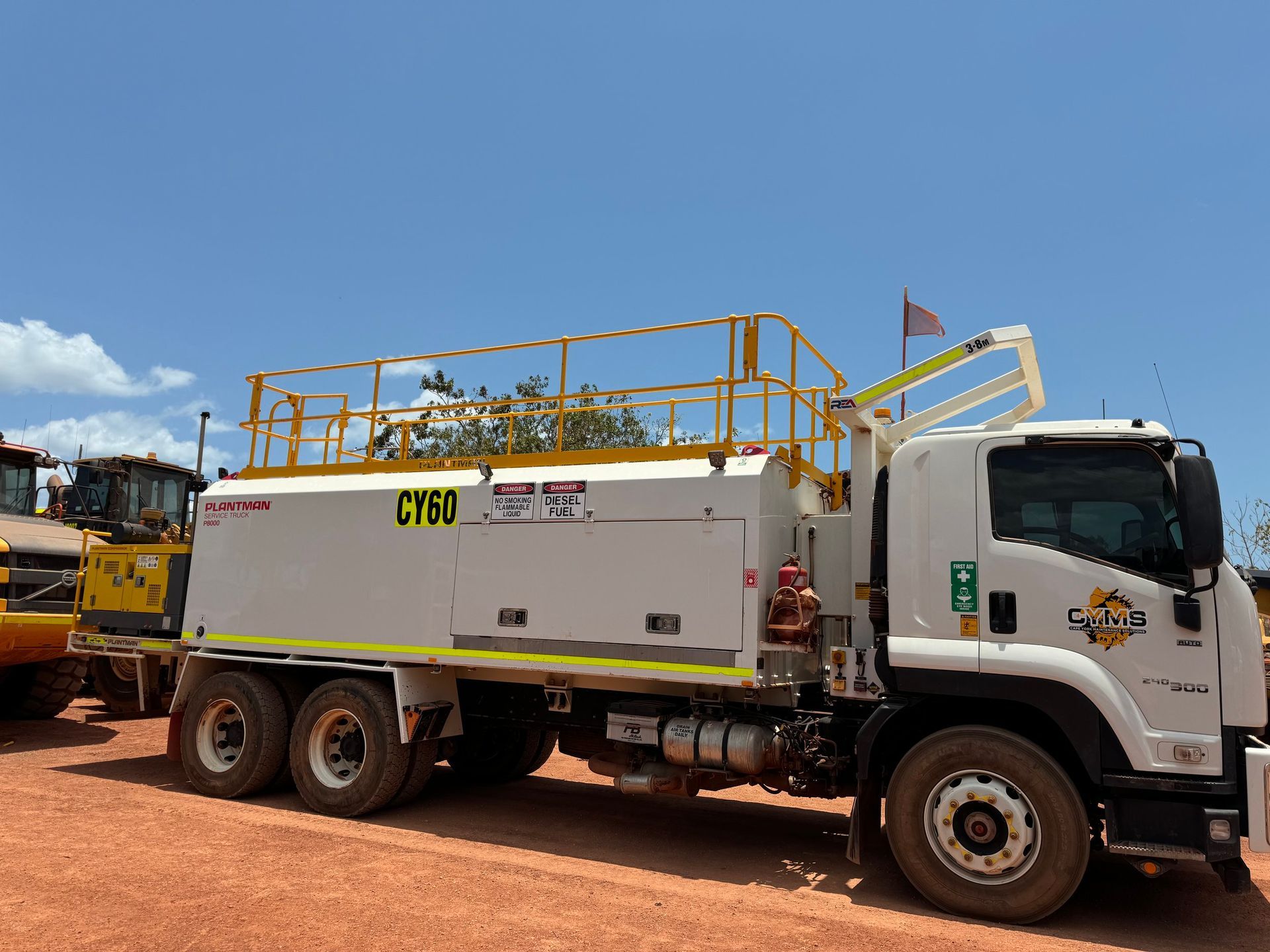 White utility truck with yellow equipment racks parked on a dirt lot under a blue sky