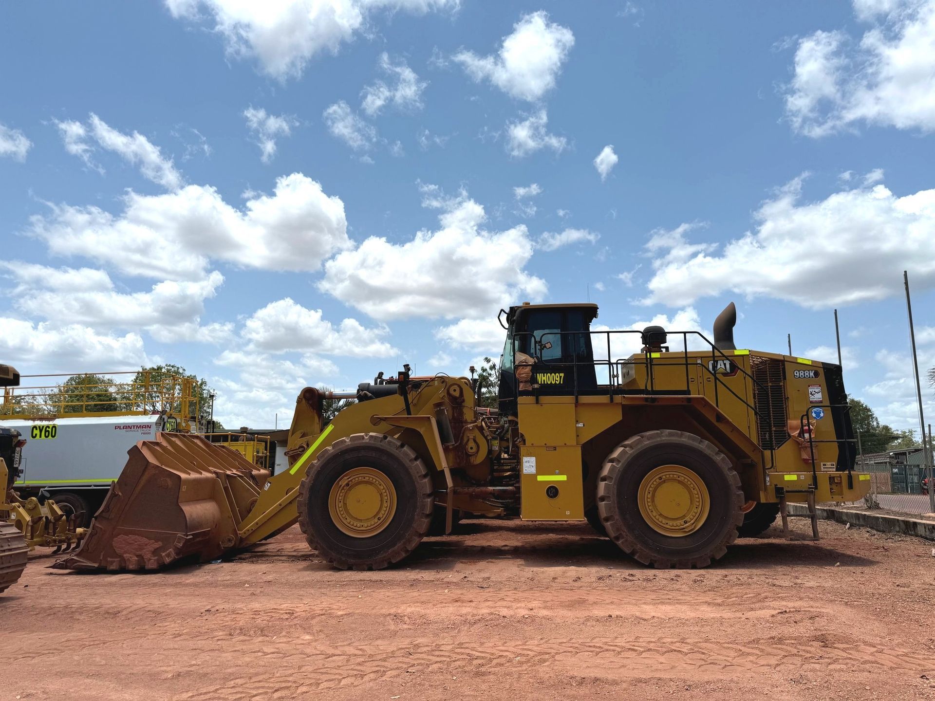 Yellow front loader on a dirt lot under a blue sky with clouds