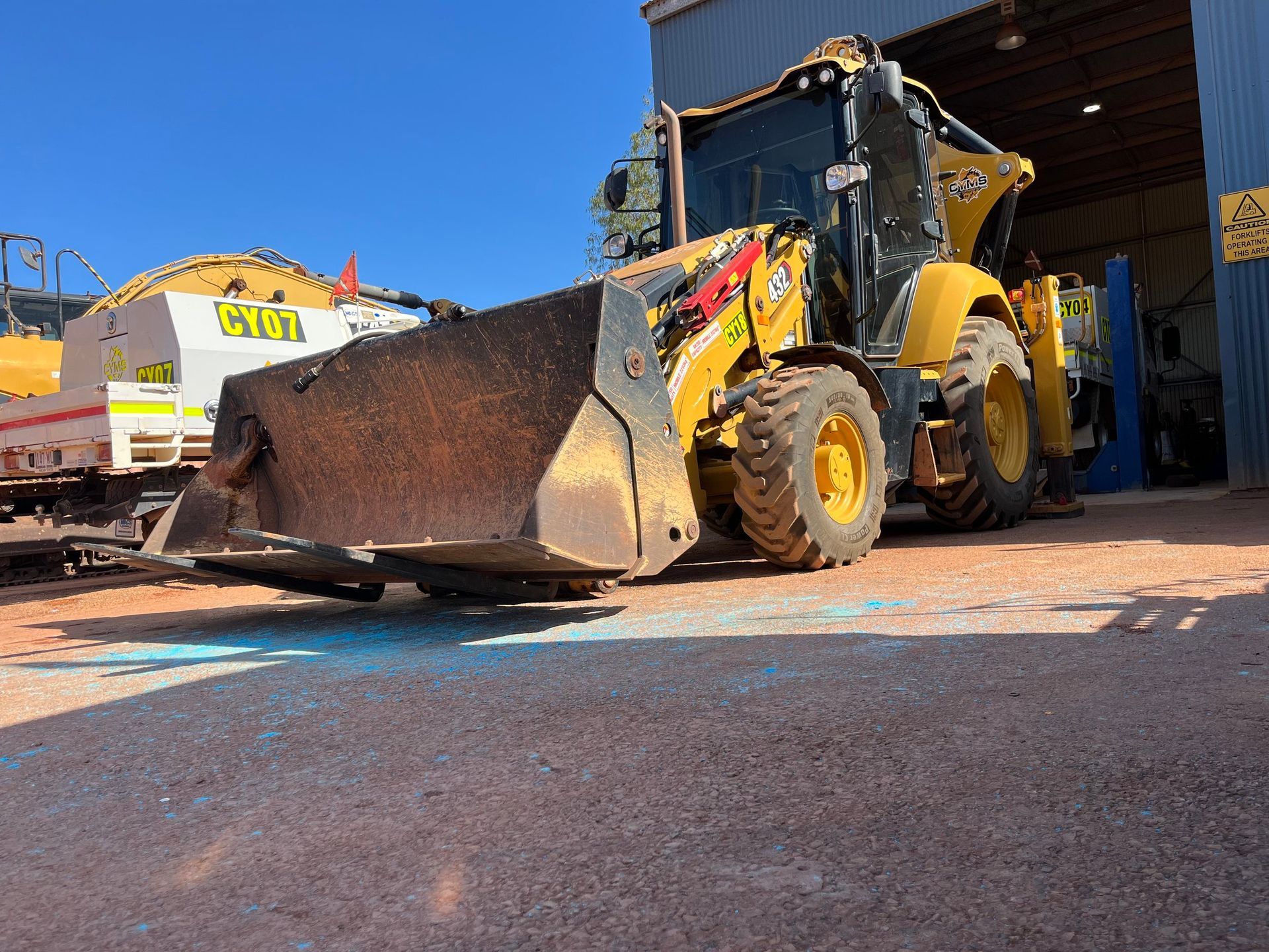 Yellow front loader with raised bucket inside a shed, on a dusty concrete floor.