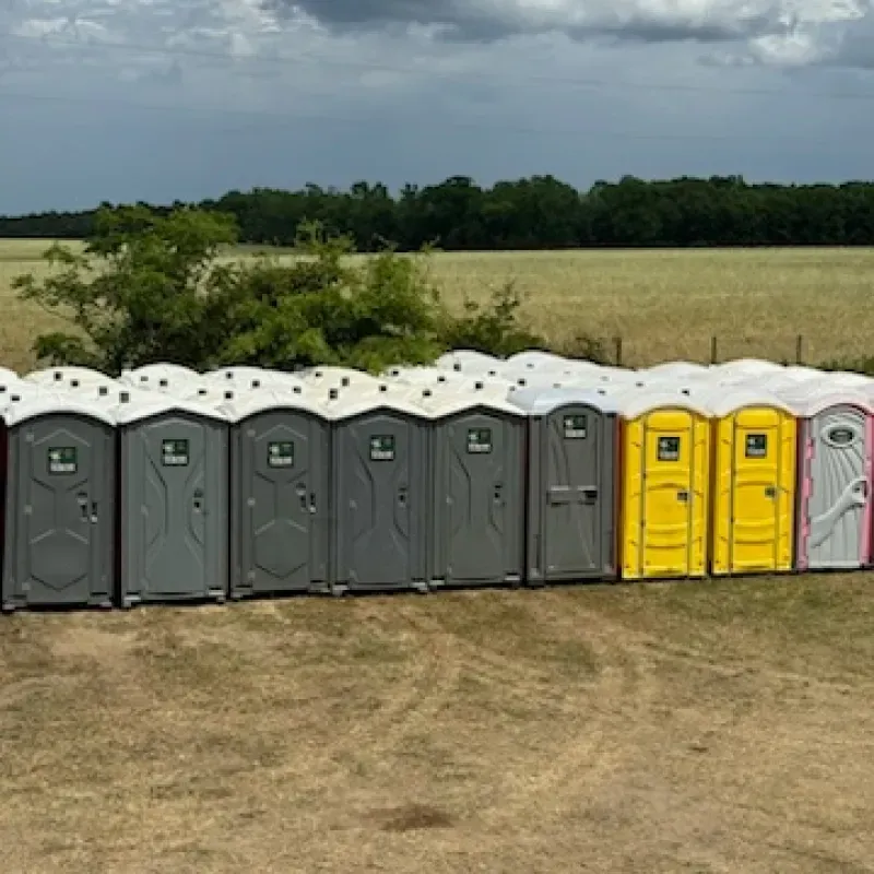 A row of portable toilets are lined up in a field.