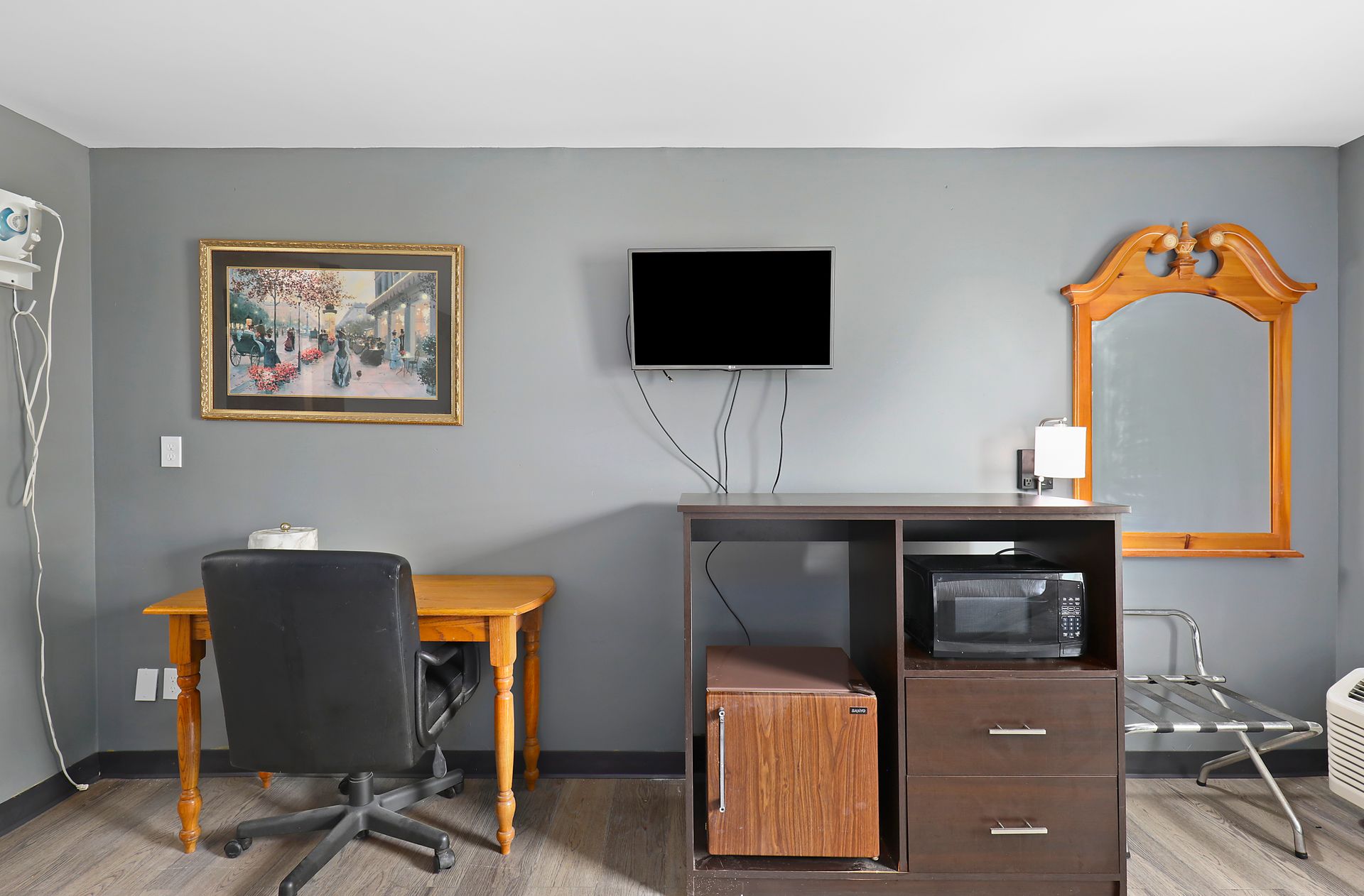A hotel room with a desk , chair , television and microwave.