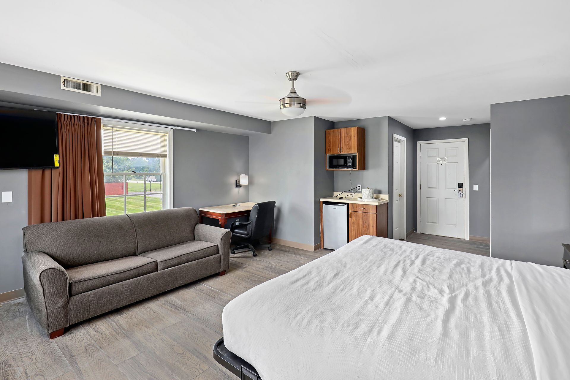 A hotel room with a king size bed , couch , desk and television.