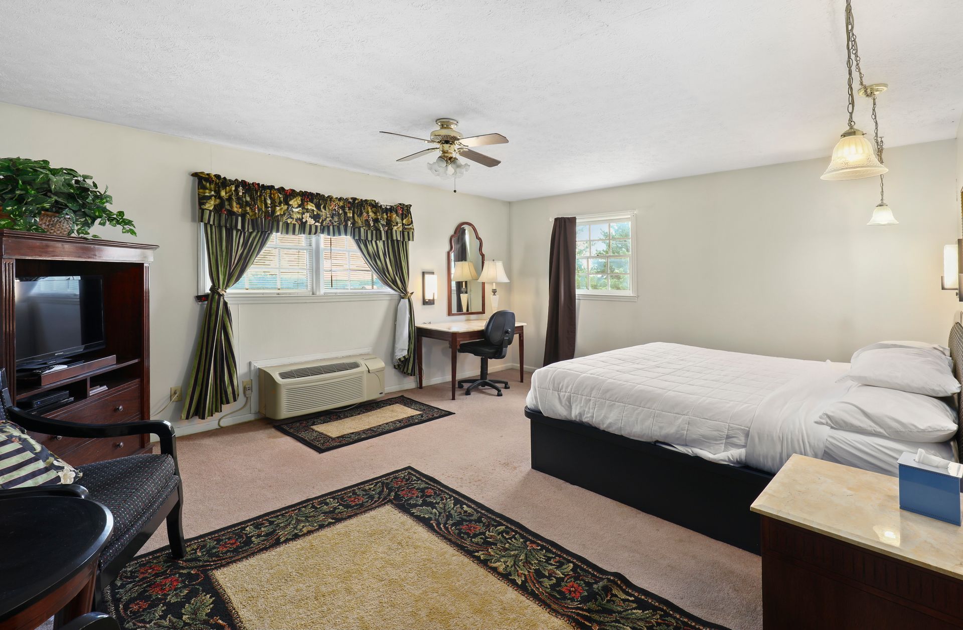 A hotel room with two beds , a desk , a television and a ceiling fan.