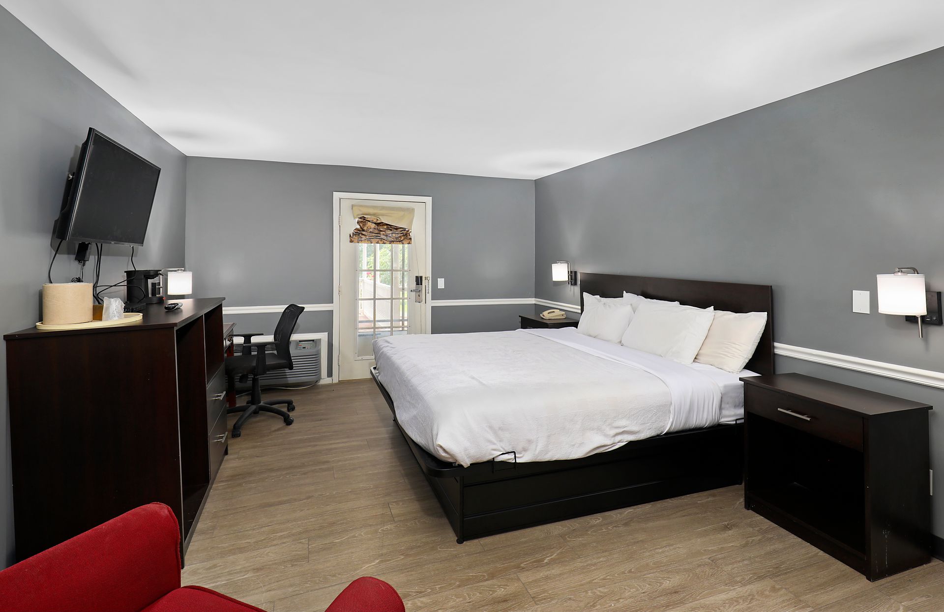 A hotel room with a king size bed , desk , chair and television.